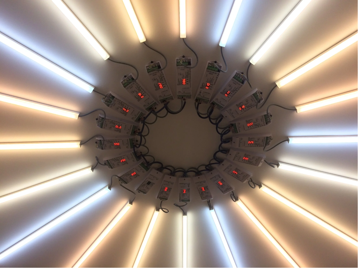 Une installation artistique ou photographique composée de tubes lumineux et de cartes électroniques ou étiquettes, disposés en cercle avec un éclairage chaud et froid.