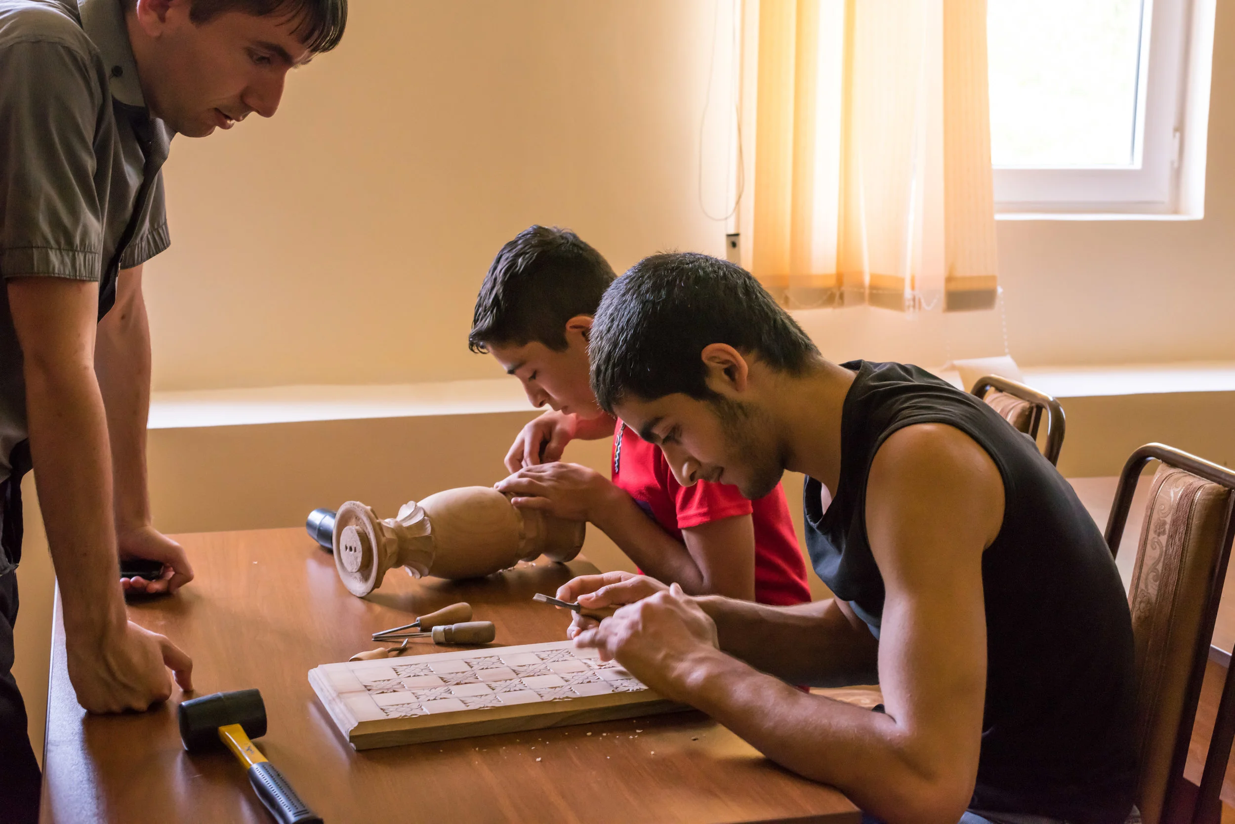 Boys carving a chessboard and vase at FAR's woodcarving hobby group in Chinchin.