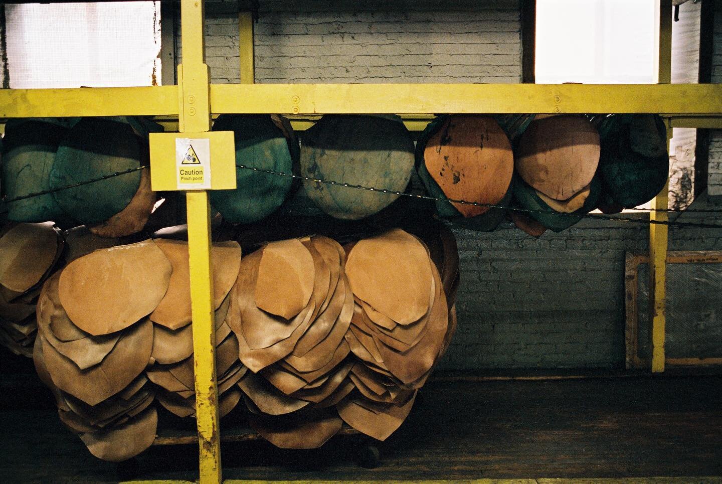 Shell cordovan hanging to air dry after receiving a dye coat. The shells are hung from sticks and move very slowly down a conveyor while warm air is blown from above. Once they reach the end they are stacked and brought back for another coat - depend