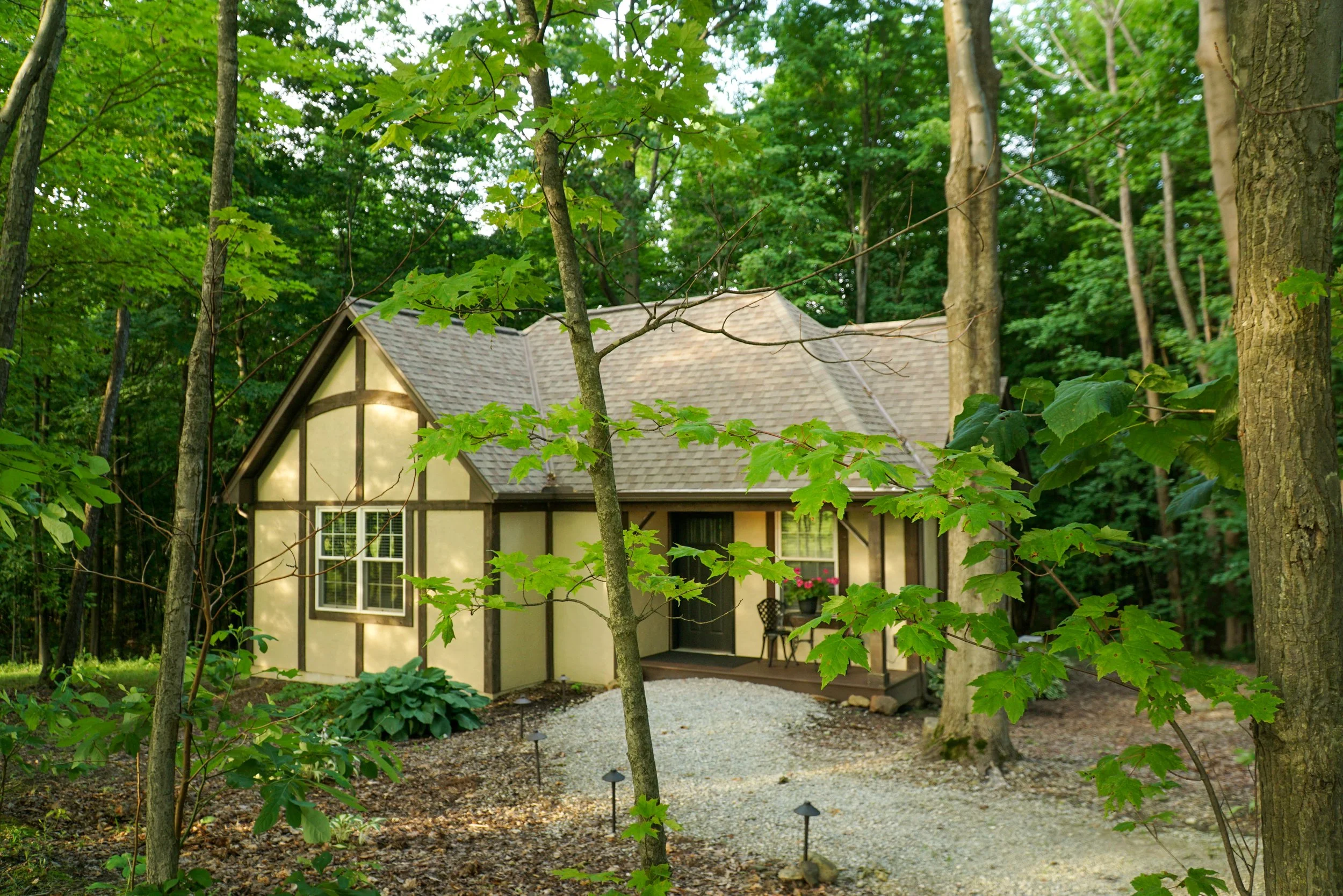 A house with Tudor-style architecture surrounded by trees and a gravel pathway in a forest setting.