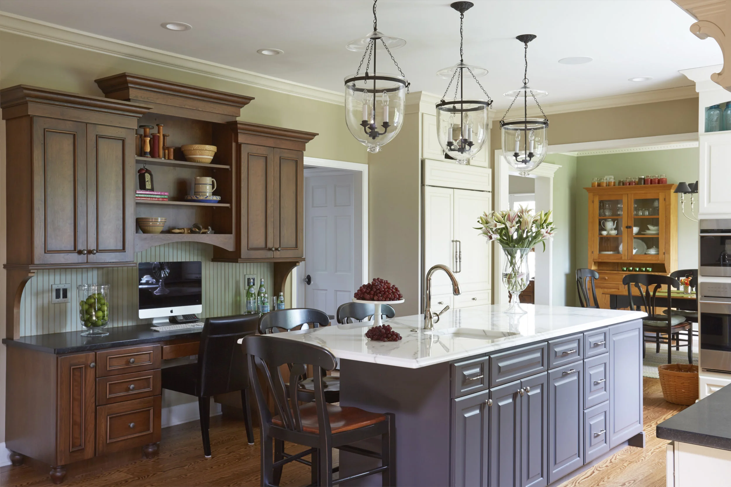 A wooden china cabinet with black countertop provides beautiful contrast to a white marble island. Design by Two Hands Interiors.