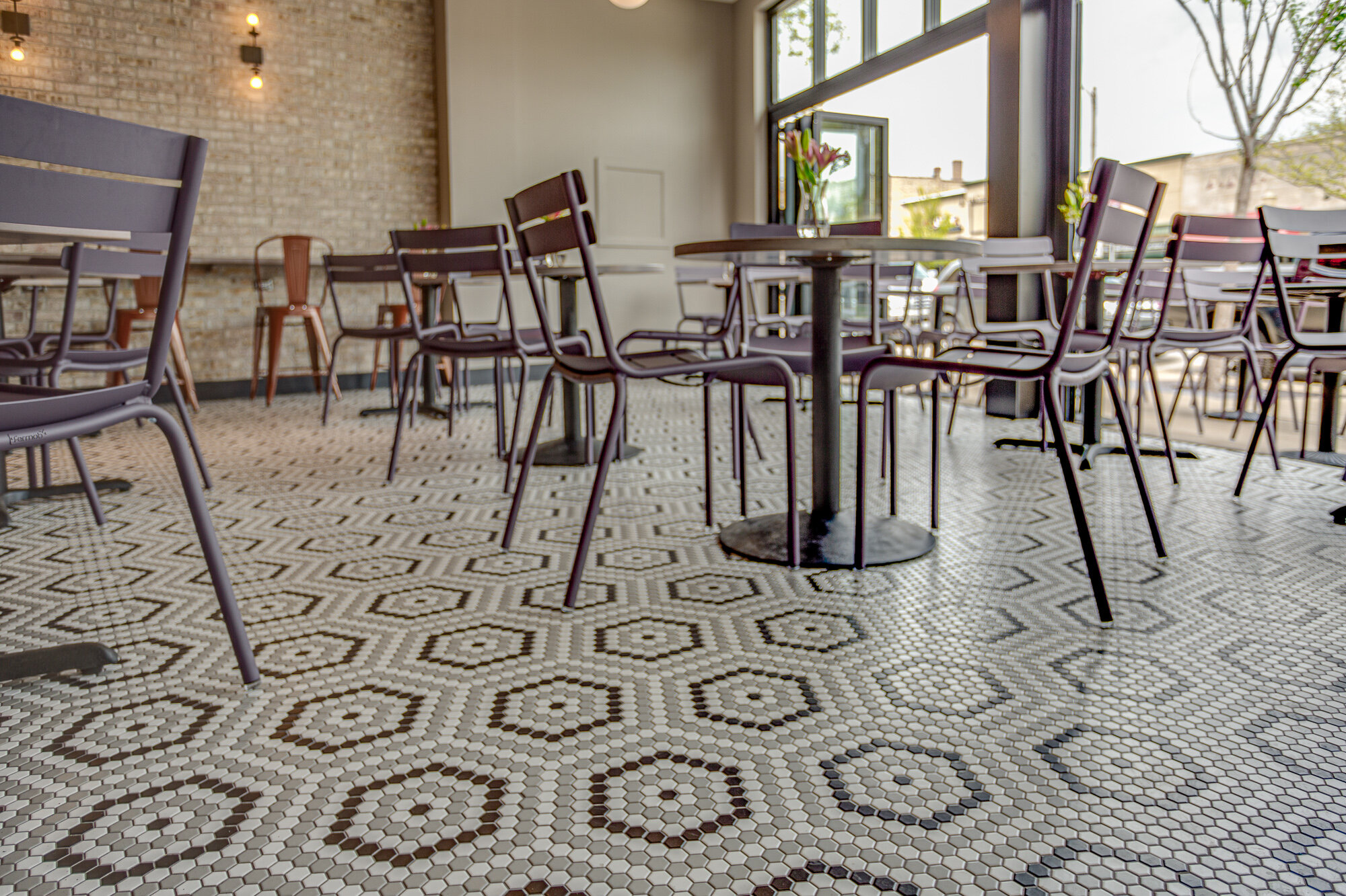 A fresh and inviting restaurant in La Grange with Ferbob furniture, a mosaic floor with hexagonal tile floor and exposed brick.