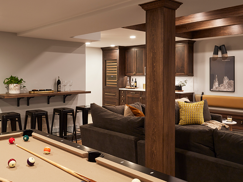 A basement play area for adults complete with custom floating side table, kitchenette with beverage fridge and warm custom shaker cabinets. Design by Two Hands Interiors.