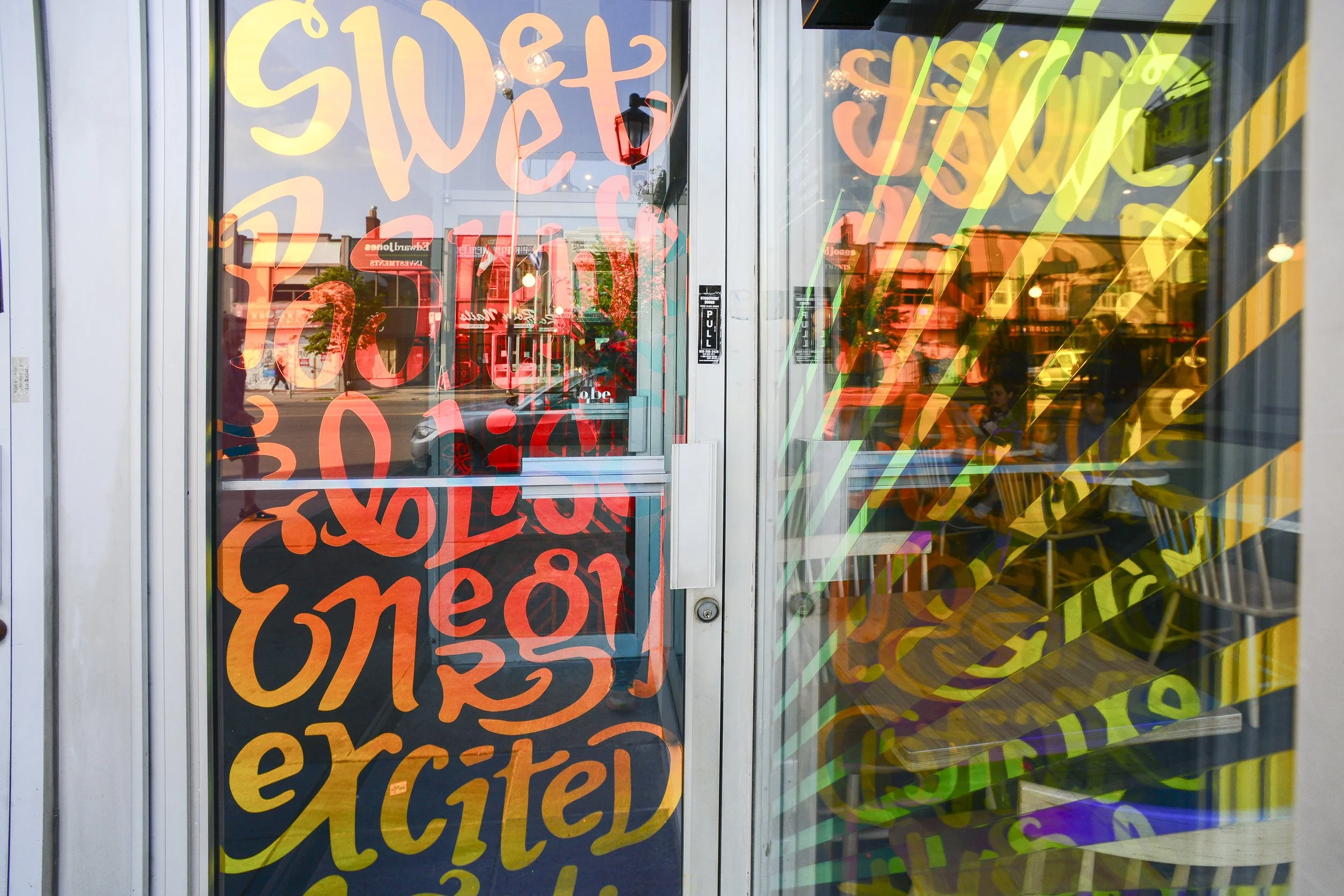 High-energy, hand-lettered window installations designed to transform a storefront into a vibrant, welcoming invitation for the community.