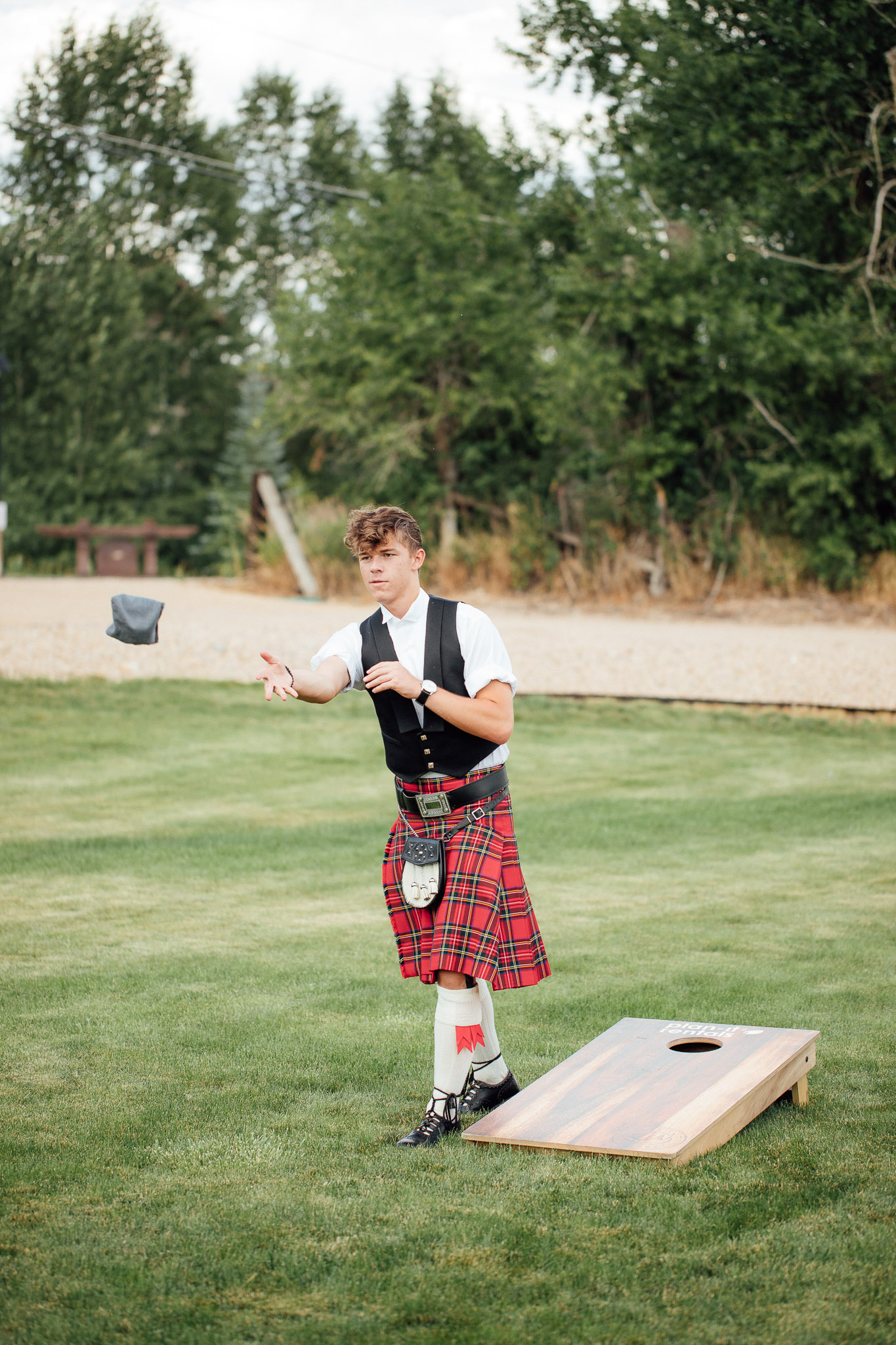 Boy in kilt plays corn hole during wedding reception