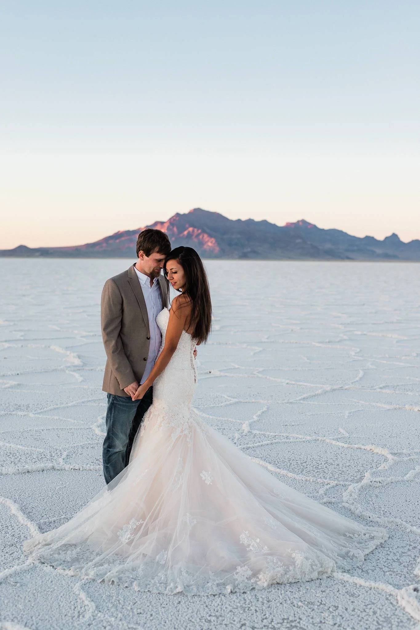Intimate wedding couple portrait on Bonneville Salt Flats in Utah with alpenglow on mountains in the background