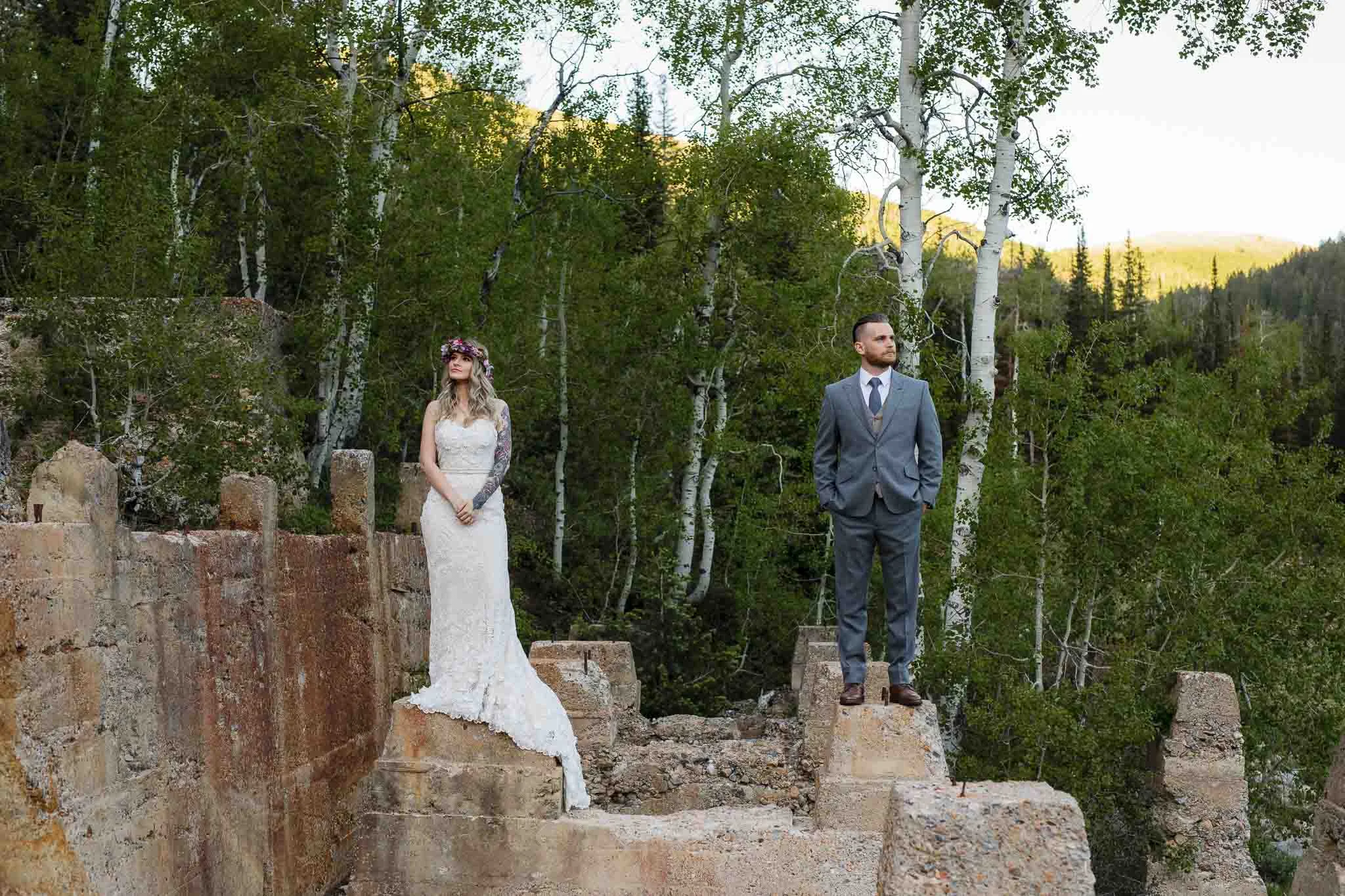 Bride and groom stand apart on ruins in forest for editorial style wedding portrait in the Wasatch Mountains in Utah