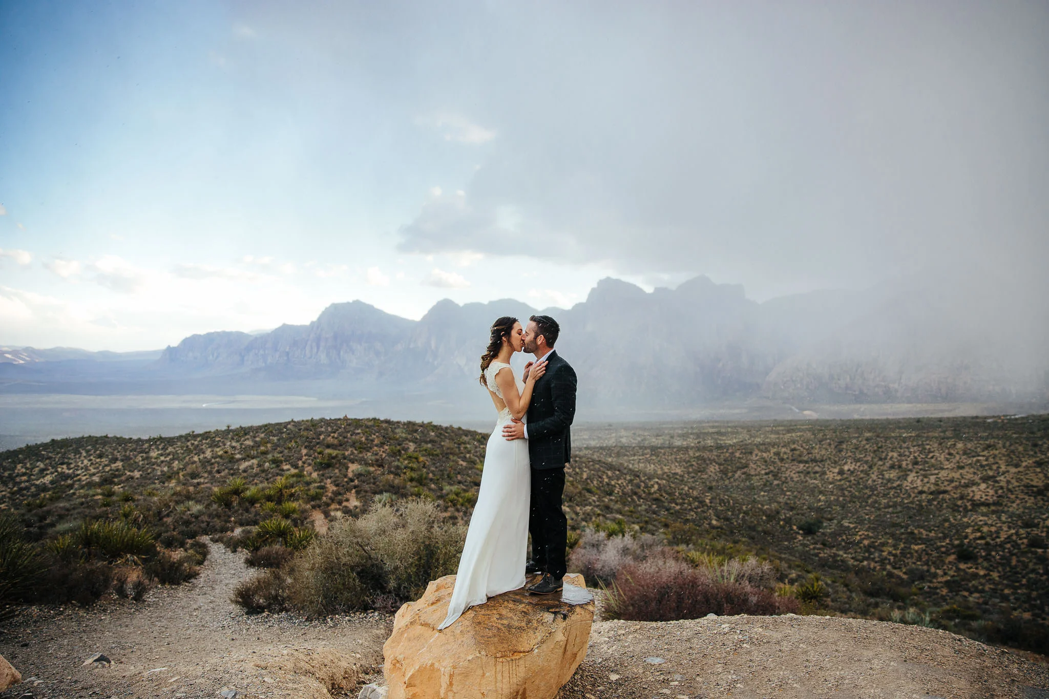 Couple stand on a rock and kiss in a rainstorm during their elopement at Red Rock Canyon, Las Vegas, Nevada