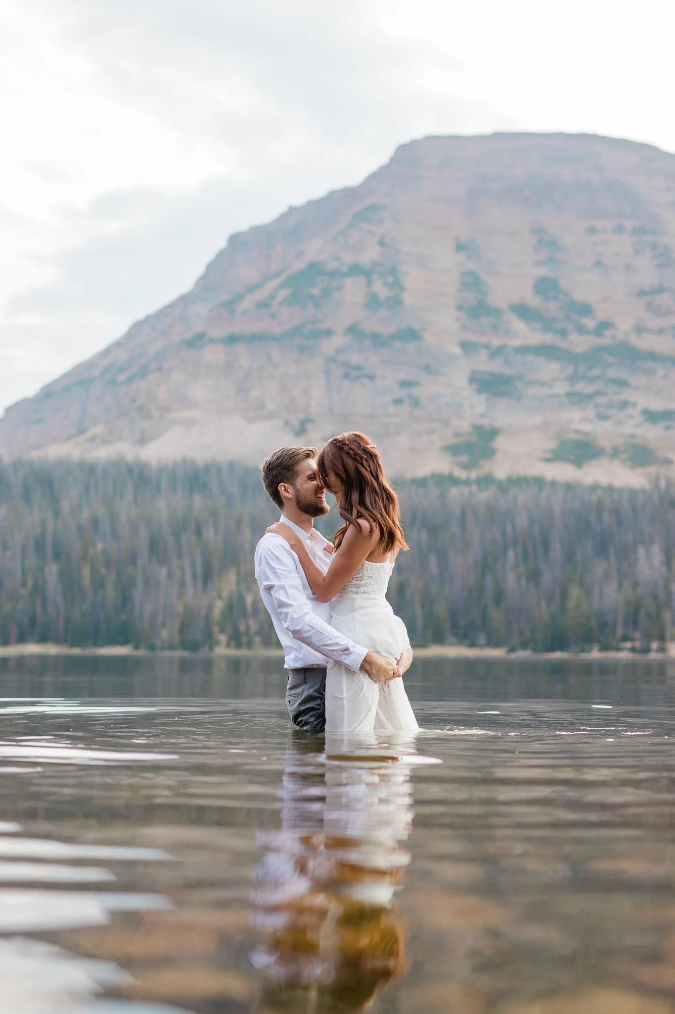 Wedding couple stand in the middle of a lake with a mountain in the background after their elopement ceremony