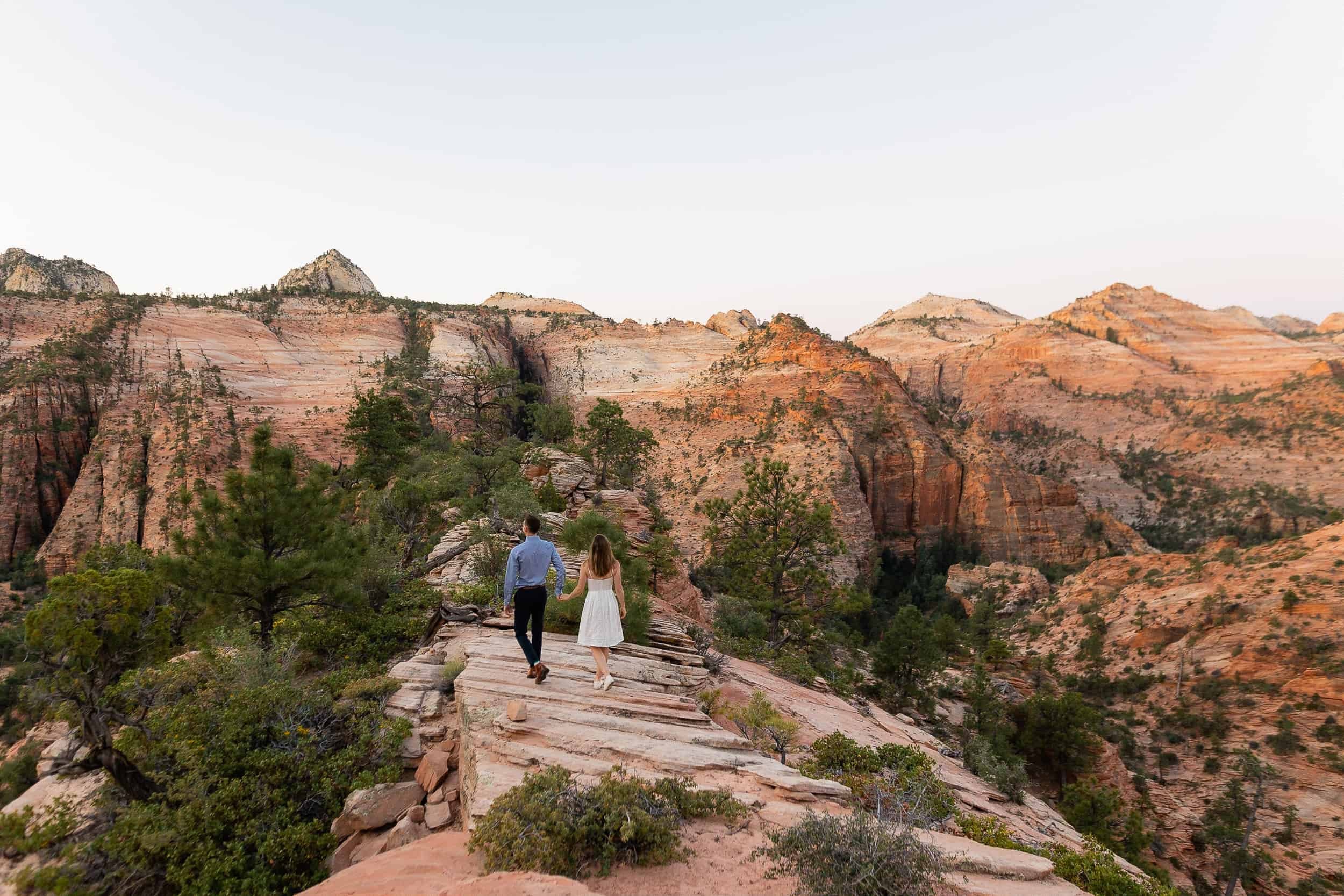 Couple walk in front of a huge view of Zion National Park during their engagement photoshoot