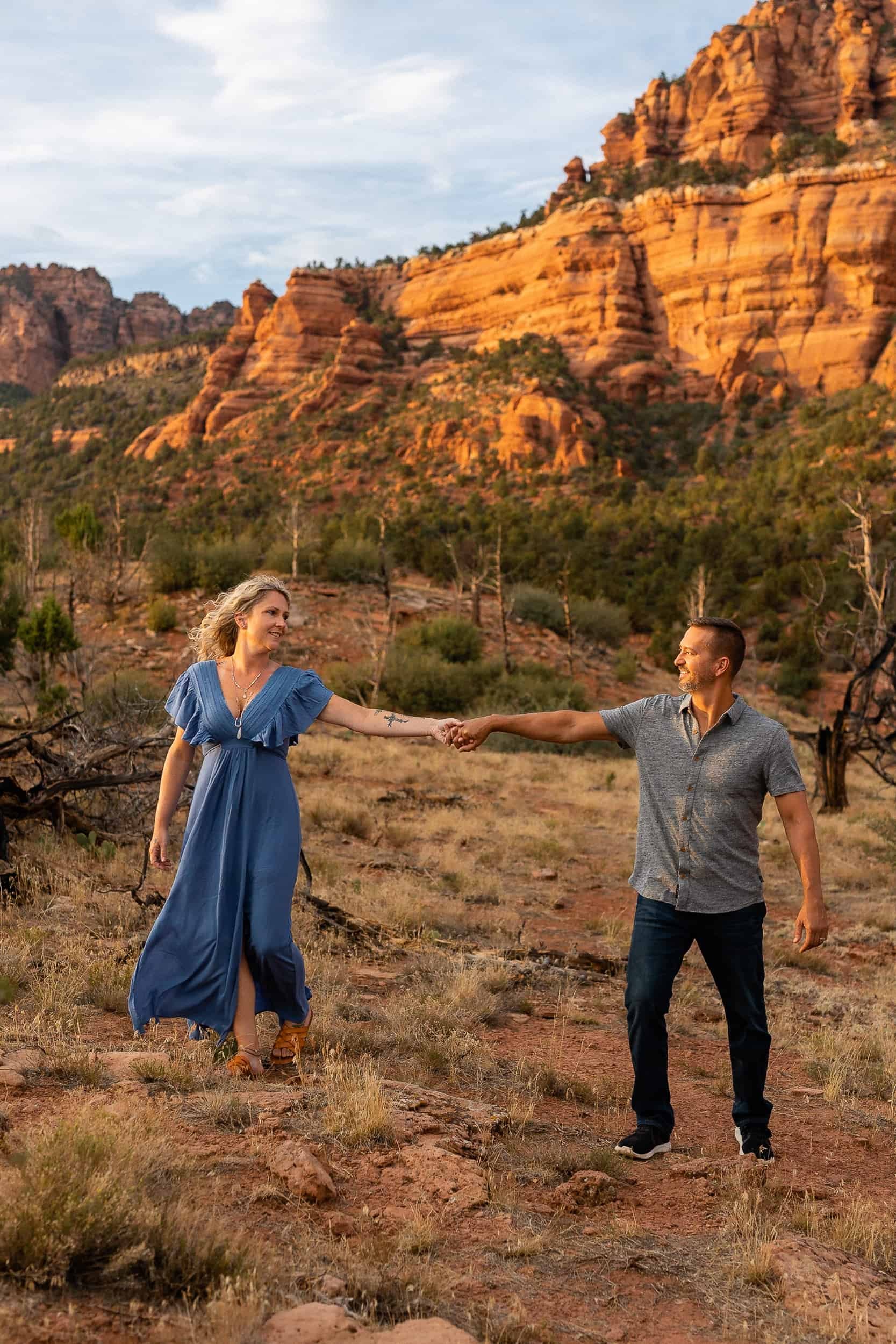 Couple walk together in front of red rock cliffs for the adventure session photographer