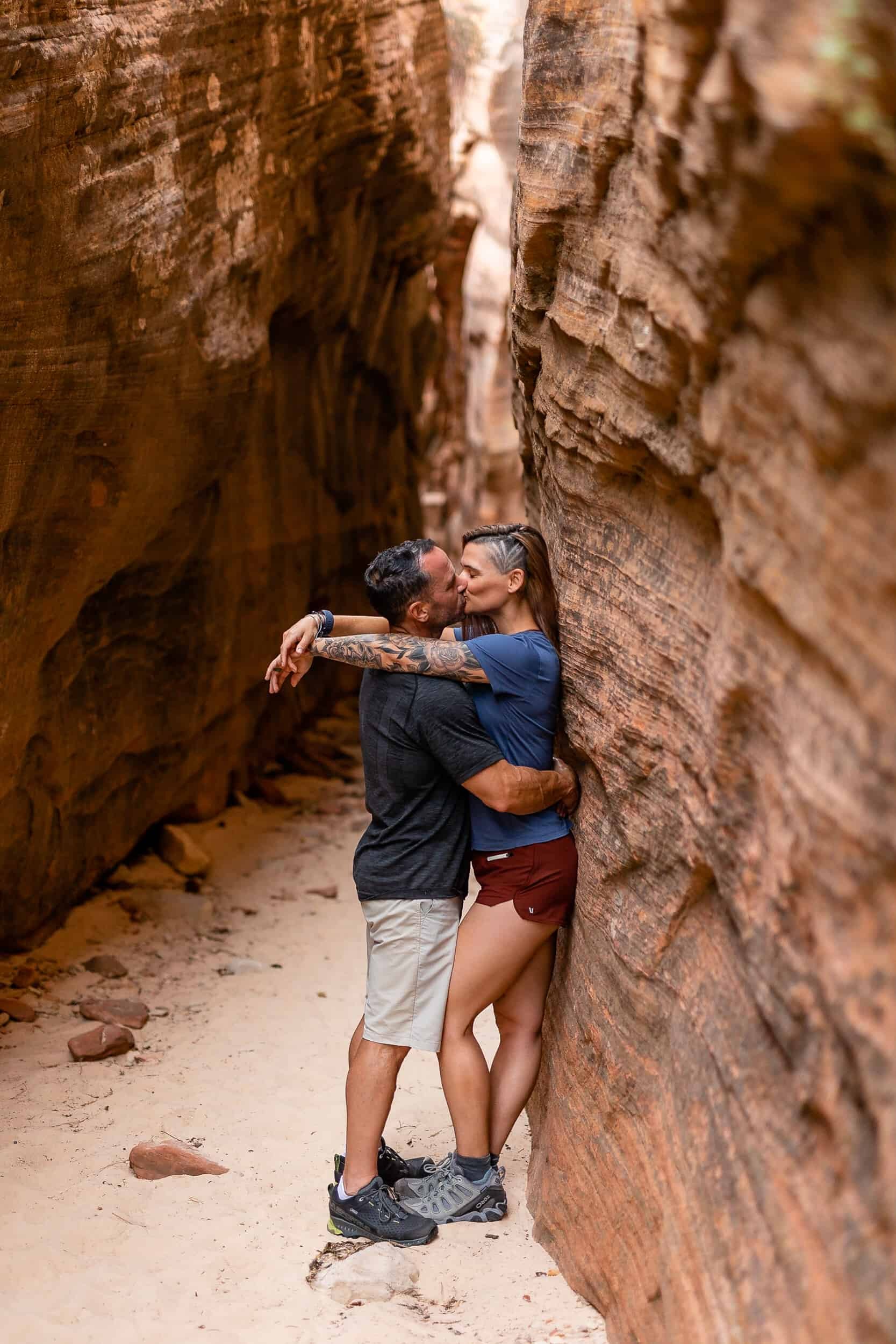 Couple kiss against slot canyon wall during their adventure session in Zion