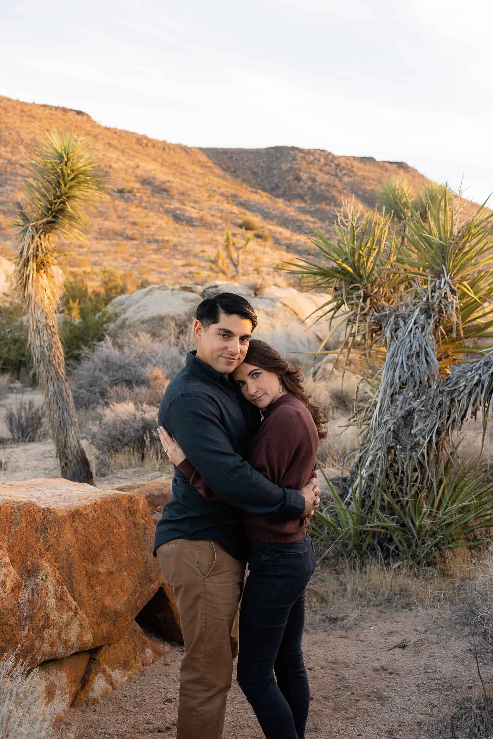 Couple embrace surrounded by cactus in Joshua Tree National Park during their adventure engagement photoshoot