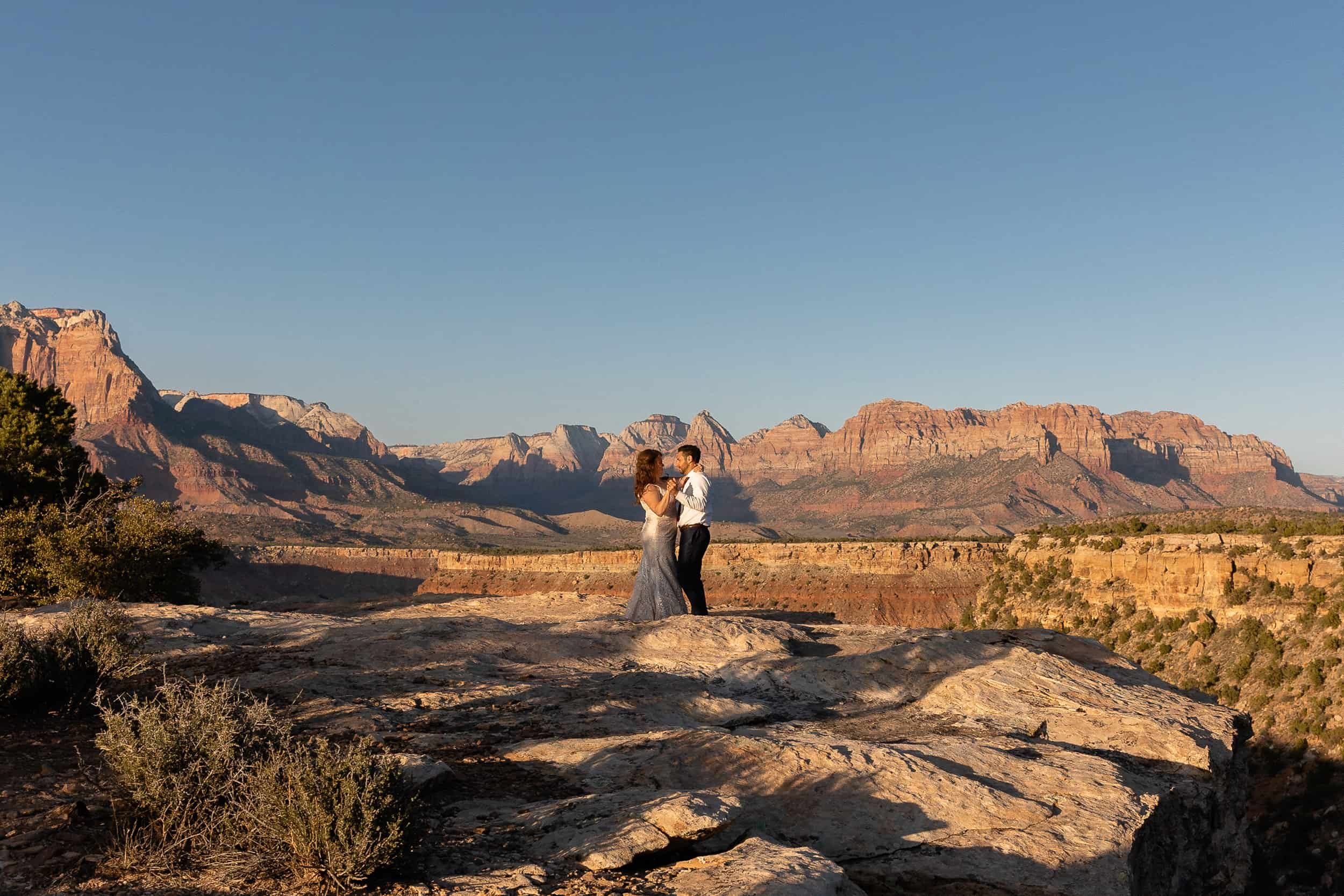 Bride and groom pose in the sunlight at sunset with Zion National Park in the background during their elopement