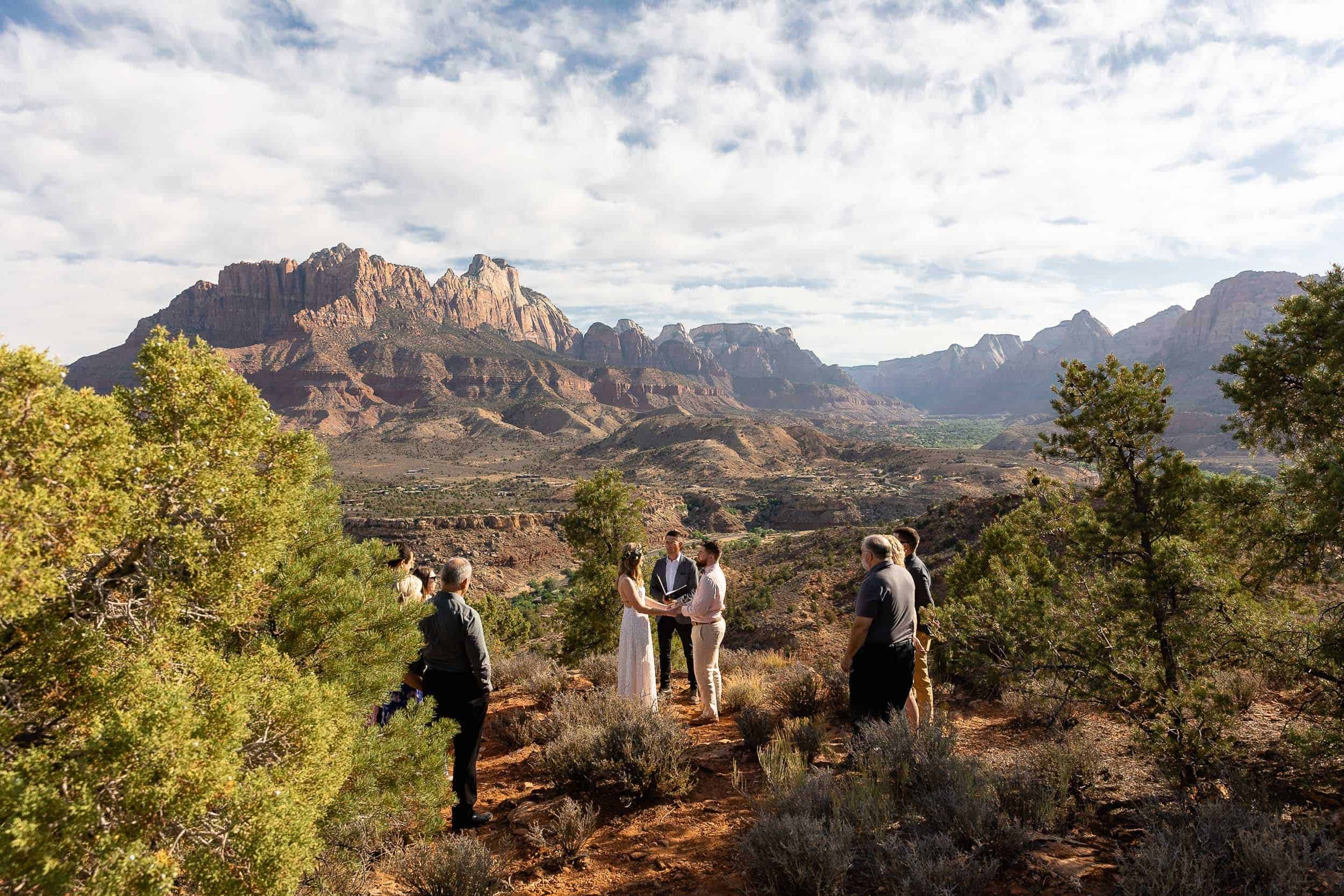 Couple hold hands with their officiant between them and their family around them during their elopement ceremony at Zion National Park in Utah