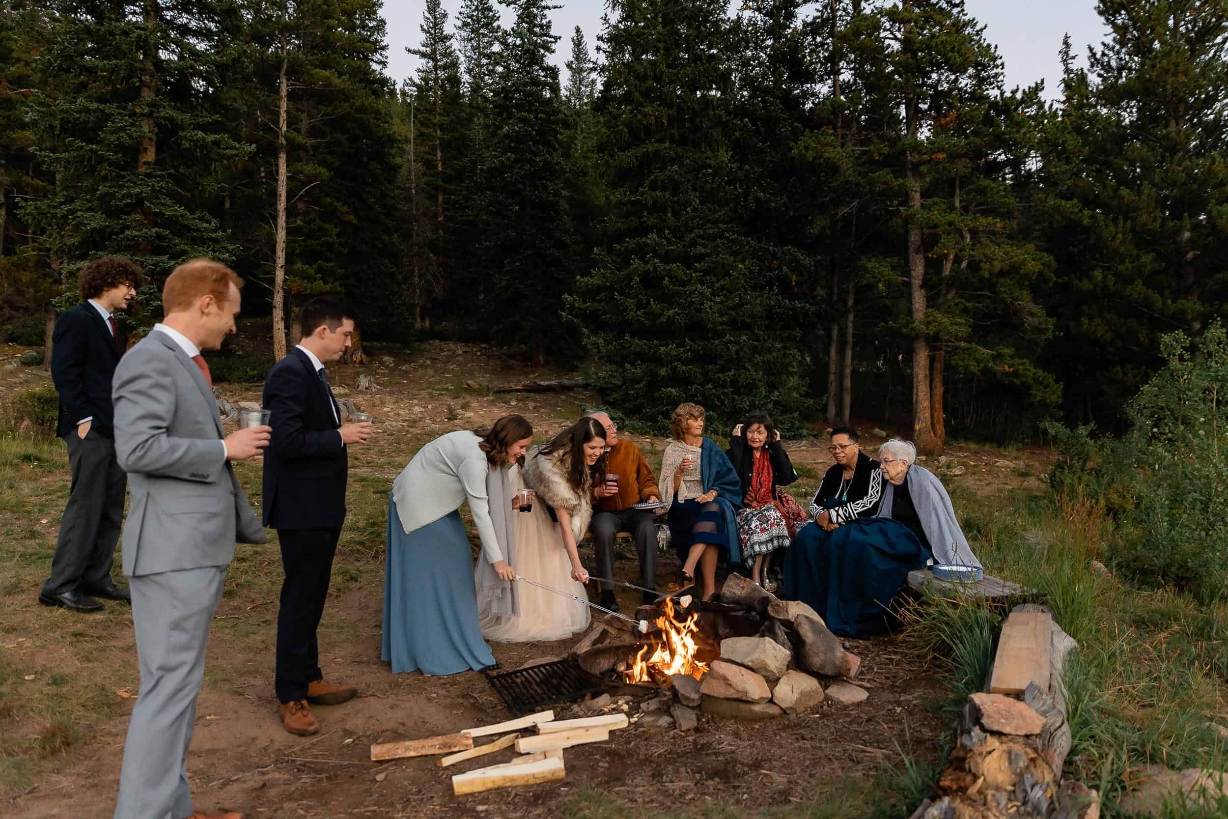 Bride roasts a marshmallow over a fire with her family around her after her Colorado elopement