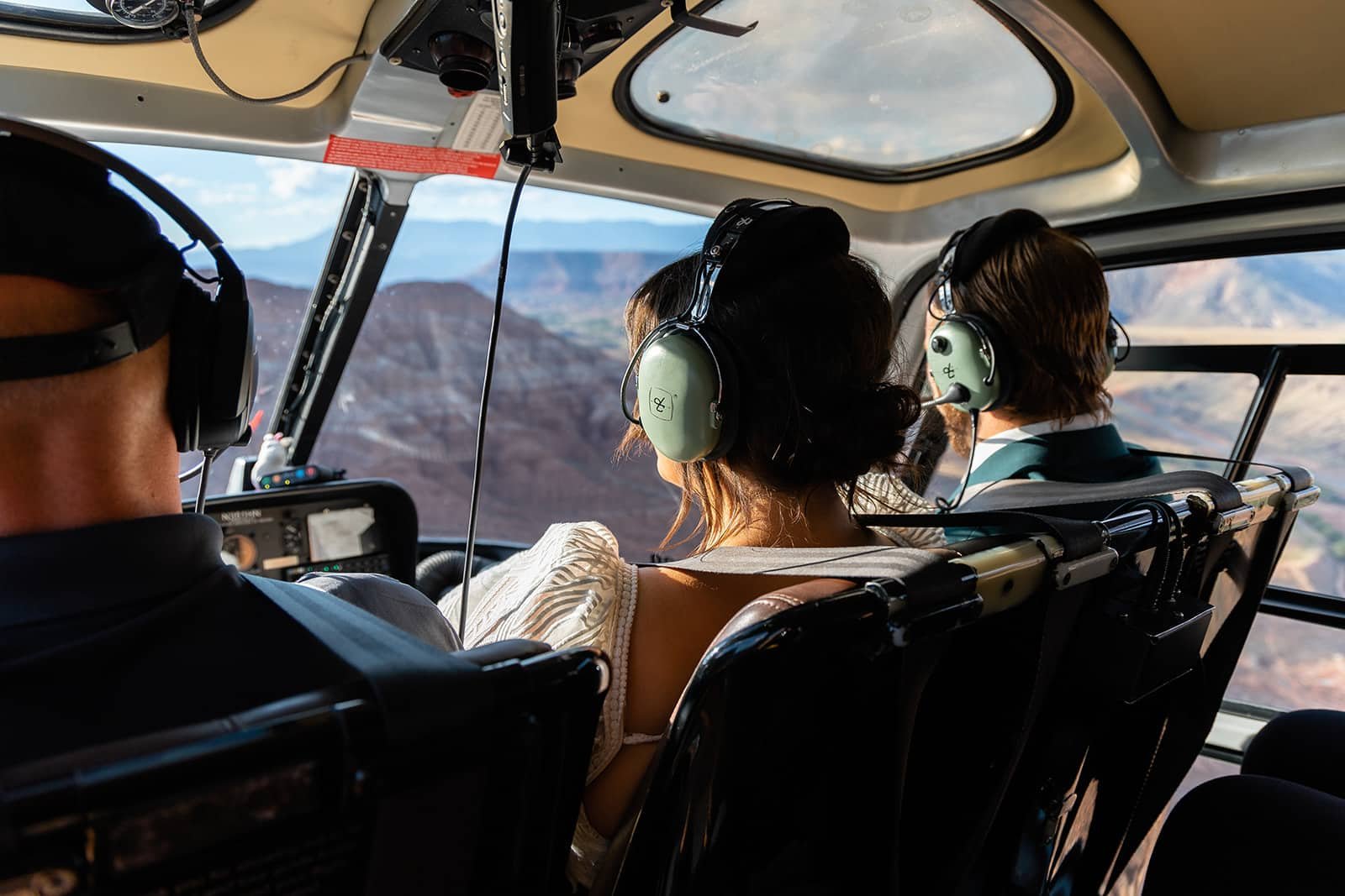 Bride and groom sit in a helicopter with headsets on and look at Zion National Park through the window