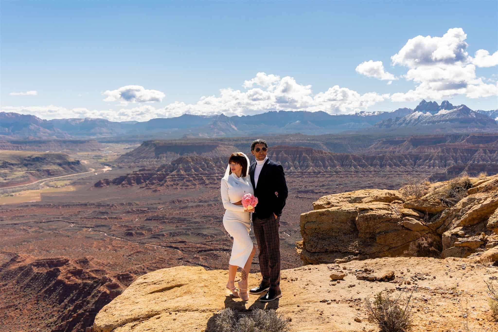 Bride and groom stand on a cliff edge in front of a view of Zion National Park during their helicopter tour photoshoot
