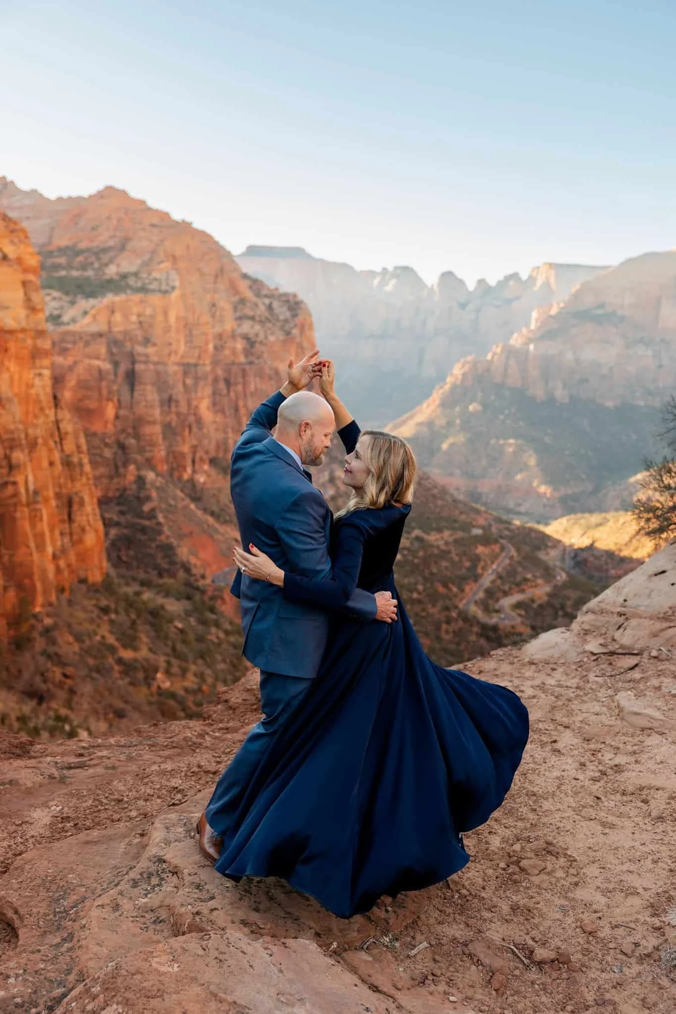 A couple dancing and embracing on a rocky terrain at sunset with a canyon landscape in the background during their Zion National Park elopement
