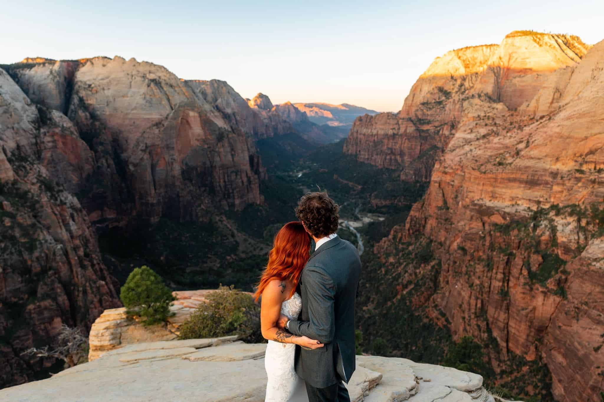 A couple embracing and looking at Zion National Park from Angel's Landing at sunrise during their elopement