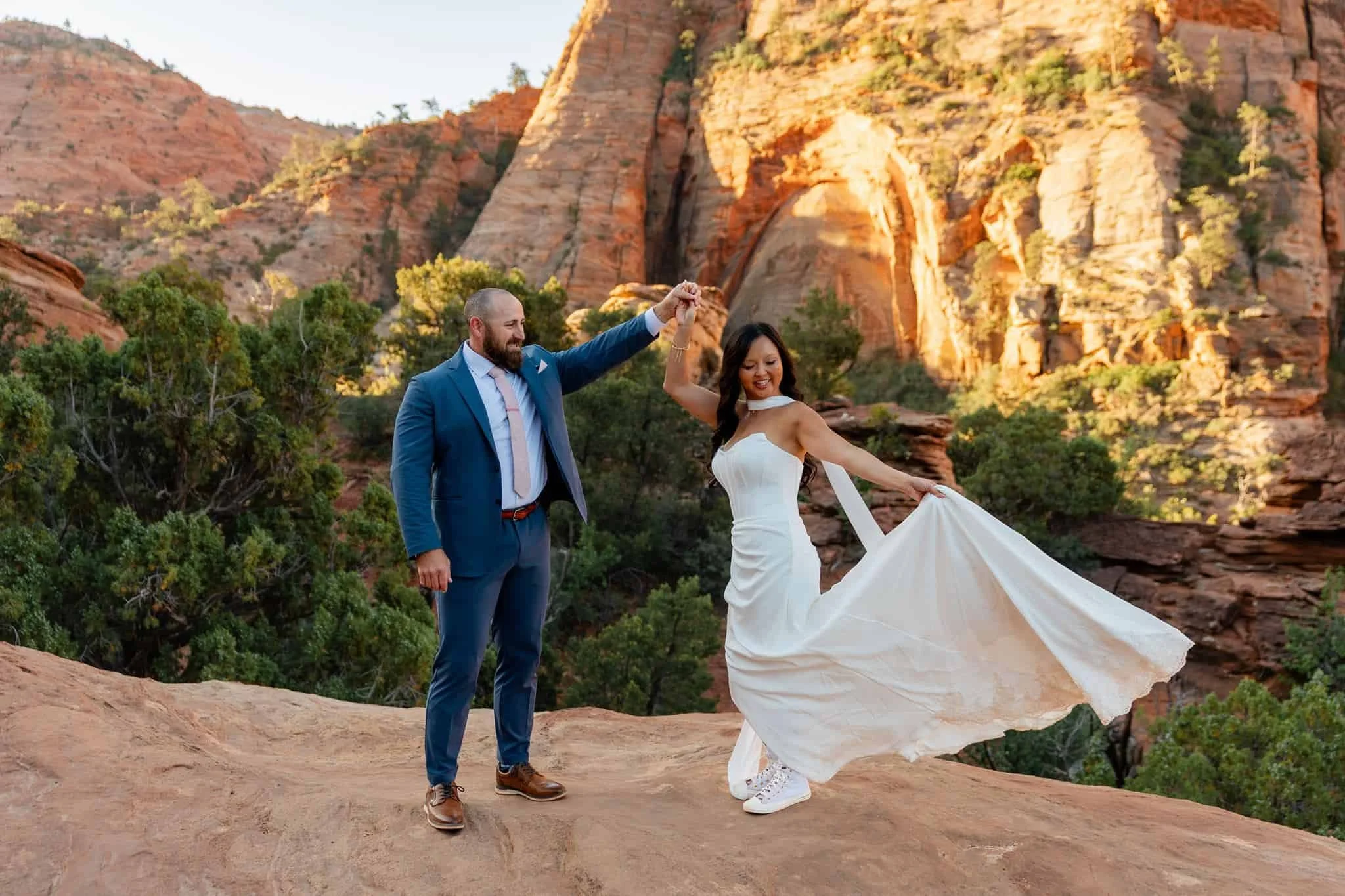 A newlywed couple dancing outdoors at sunset in a canyon with red rock formations and green vegetation during their zion elopement