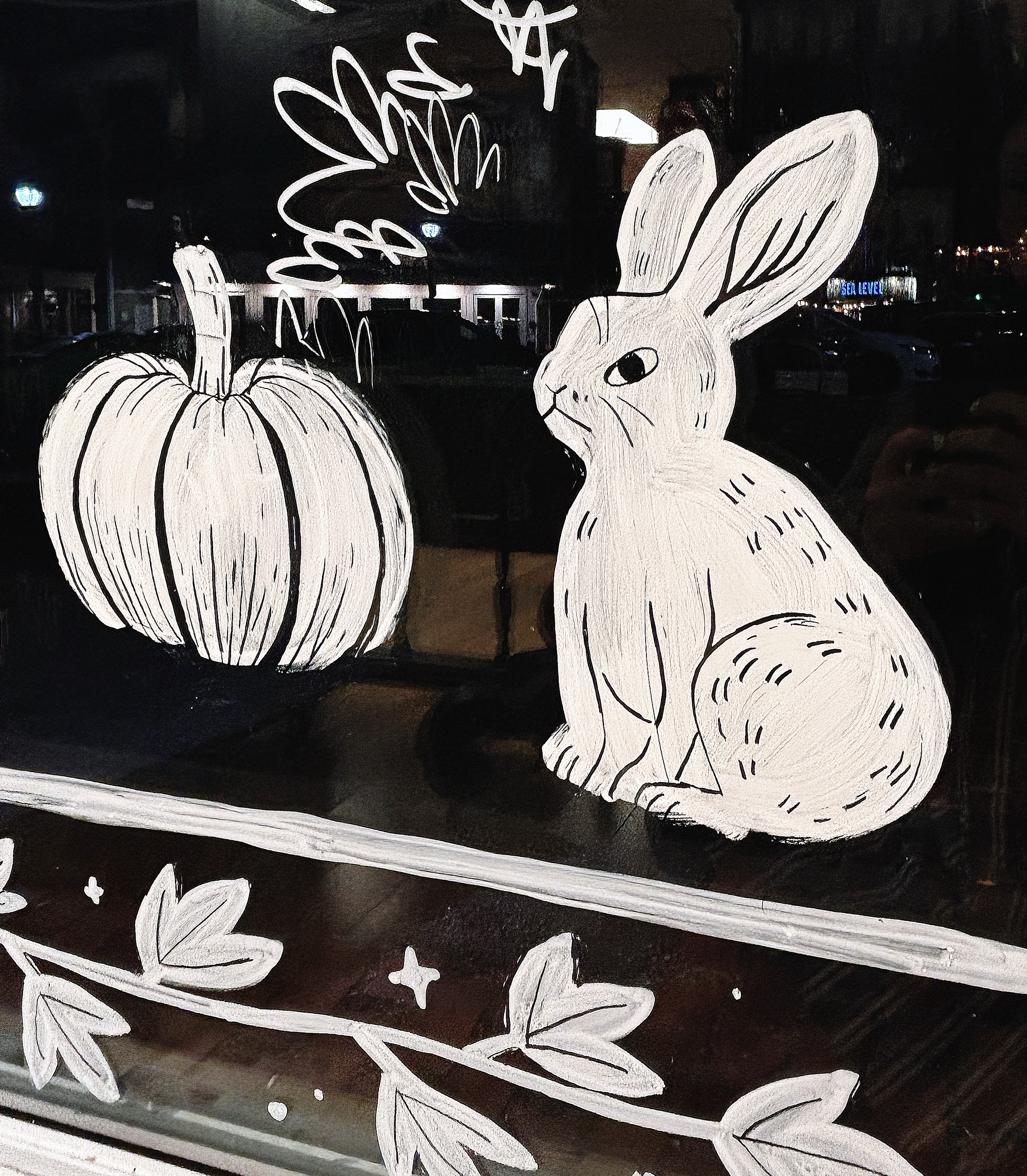 A pumpkin and rabbit, hand-painted in white paint on a glass window.