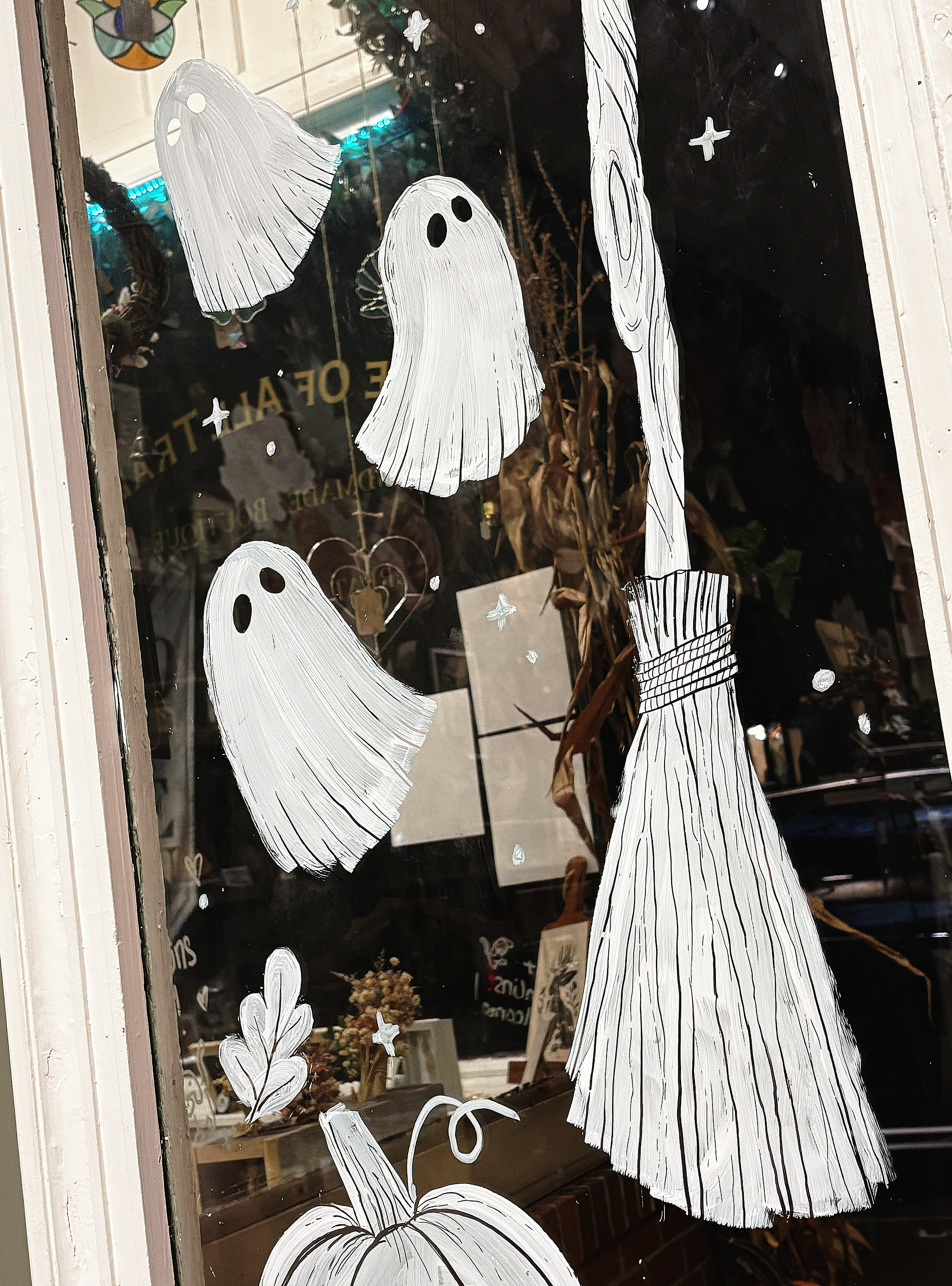 Hand-painted white ghosts, pumpkins, and a broom on a glass door.