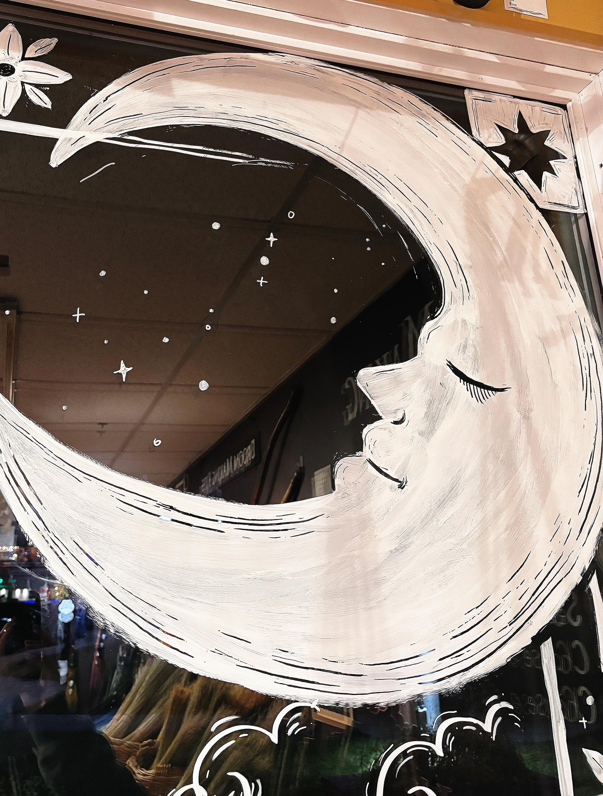 A mirror with a painted moon and stars, featuring a crescent moon with a woman's face painted inside, surrounded by clouds and small star details.