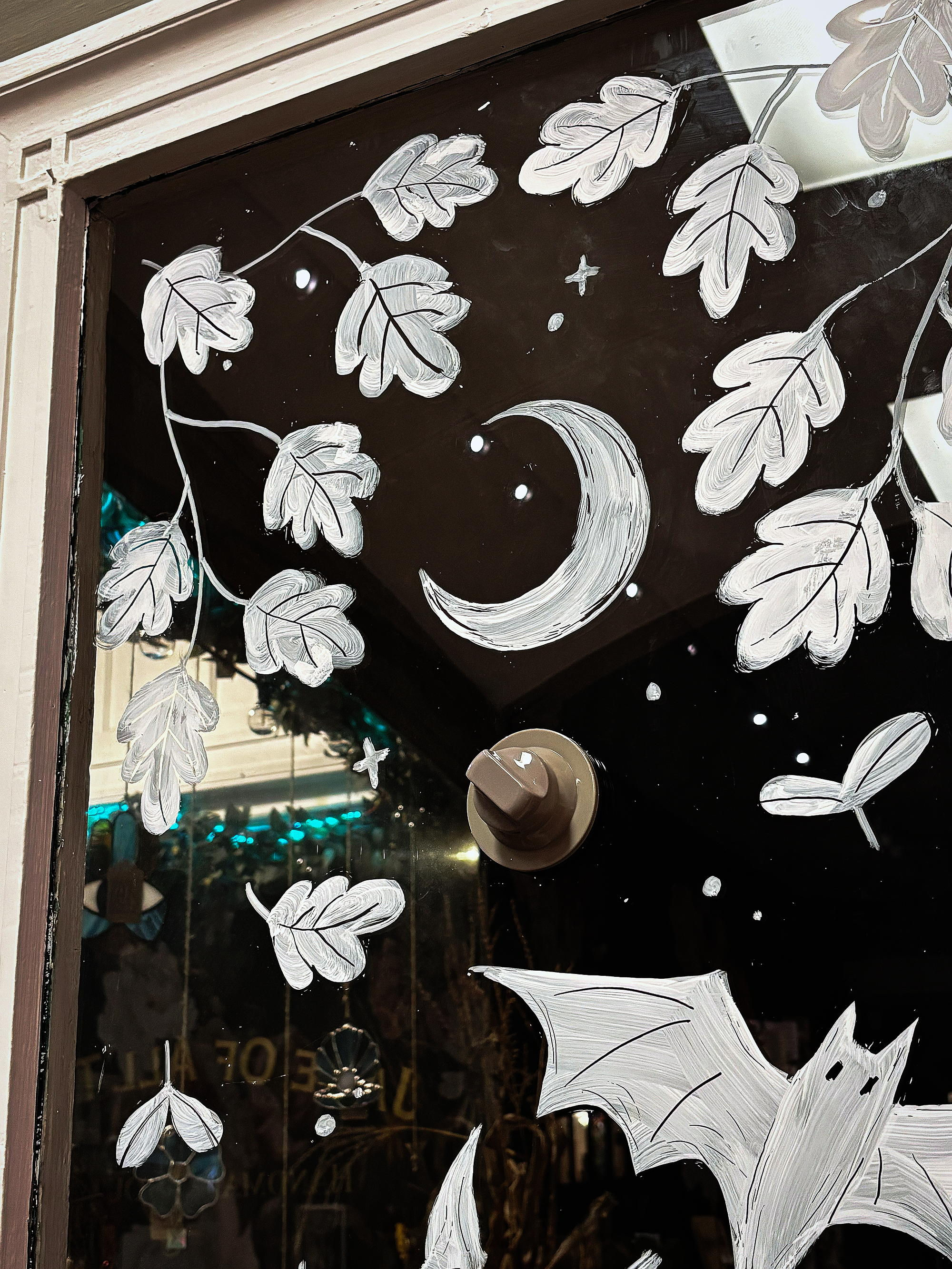 Glass window with with hand-painted white leaves, moon, stars, and bats.