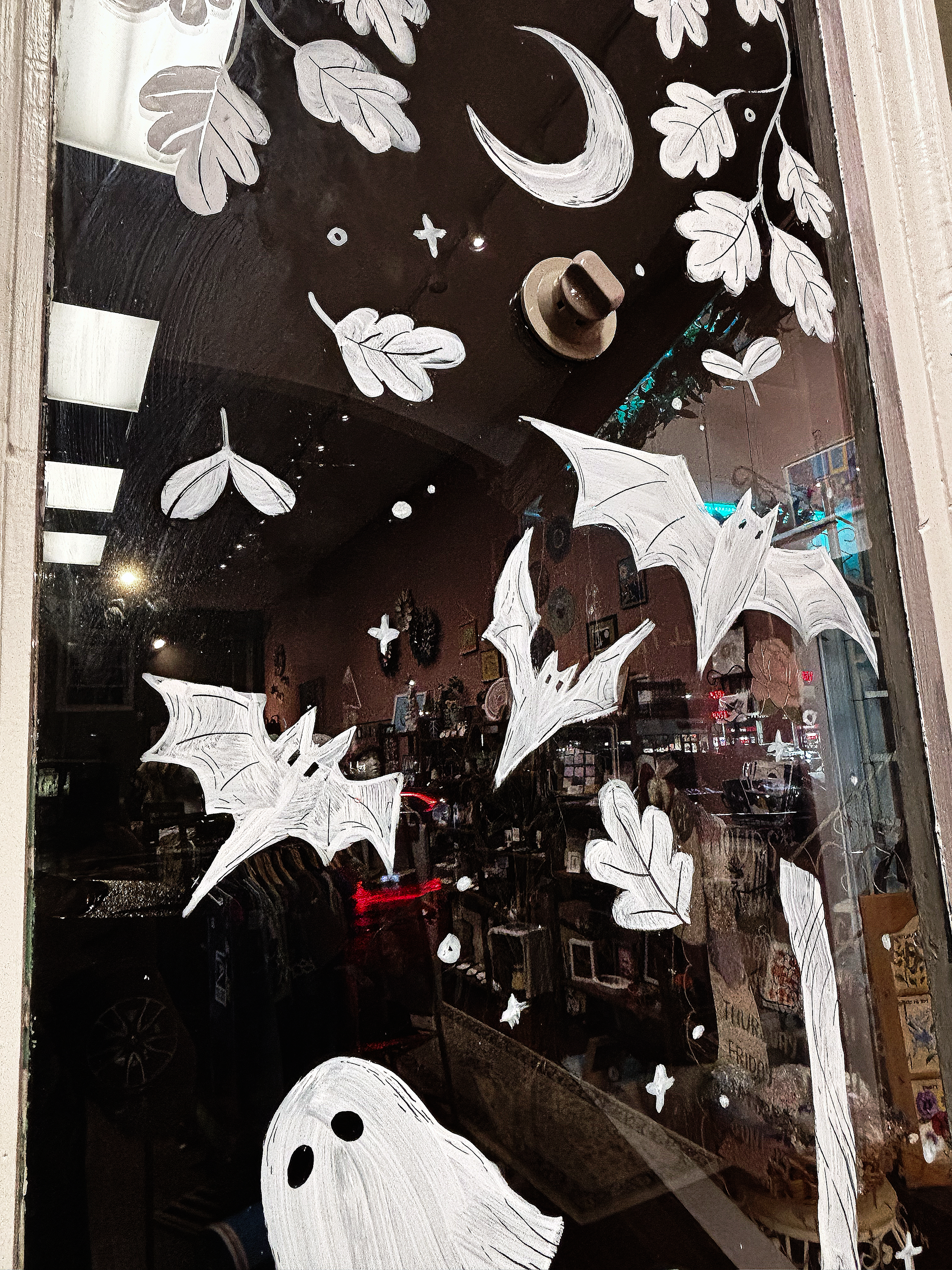 Hand-painted ghost and bats, floral designs, a crescent moon, stars, and other Halloween-themed illustrations on a glass door.