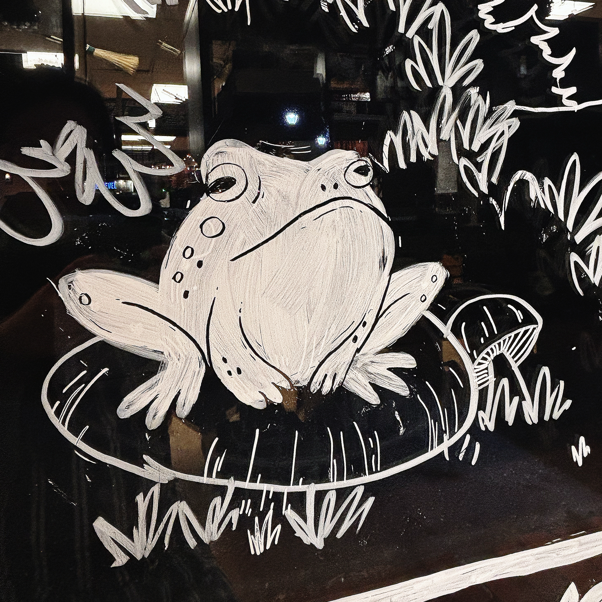 A frog on a mushroom, hand-painted in white paint on a glass window.