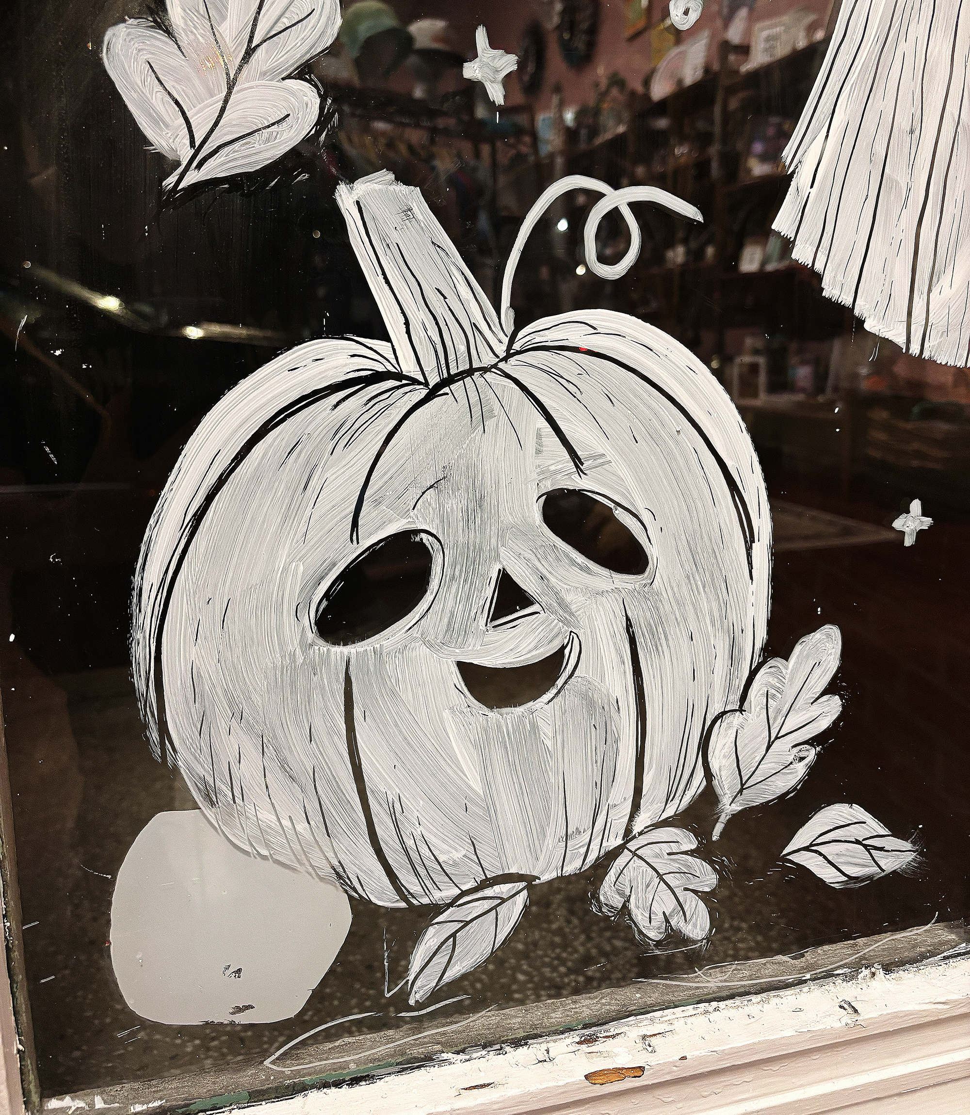 A painted white pumpkin with leaves and stems on glass door.