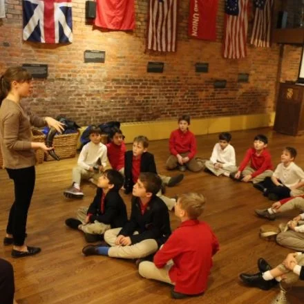 Group of school children sitting on the floor in front of an adult educator in the Museum's Davis Education Center.