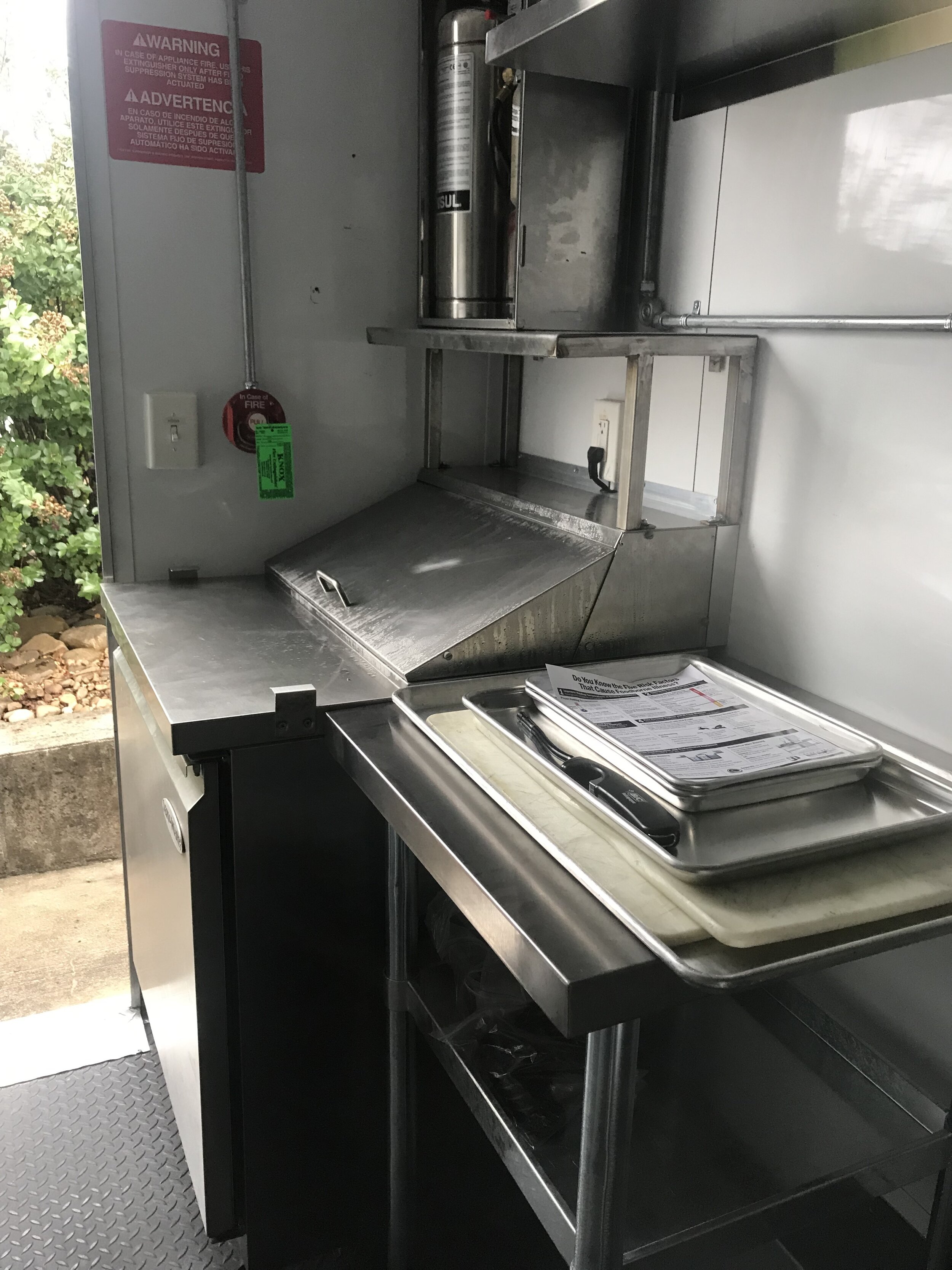  The sandwich station is above an under-the-counter refrigerator. A full-size refrigerator is at the other end of the mobile kitchen.  