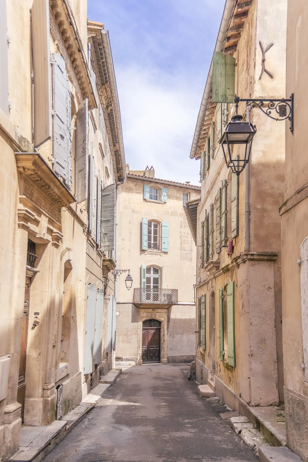 Quiet street in Arles lined with pastel shutters and golden Provencal facades