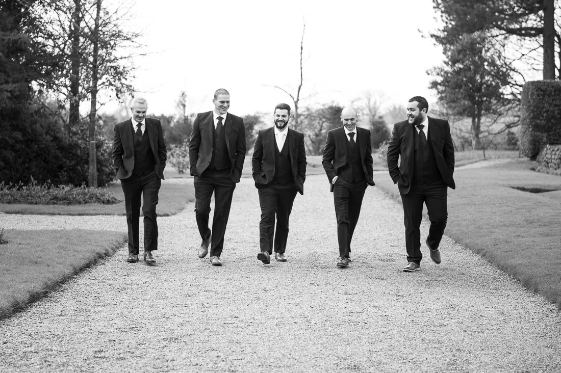 Natural black and white photo of the groomsmen walking together outside at Eaves Hall