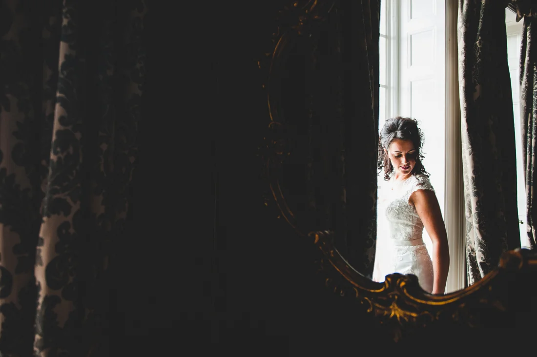Documentary photography of the bride as she stand by the window.