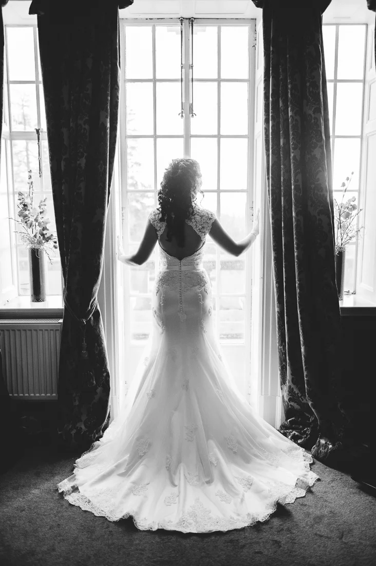 Full length shot of the brides dress as she stands in front of the window at Eaves Hall