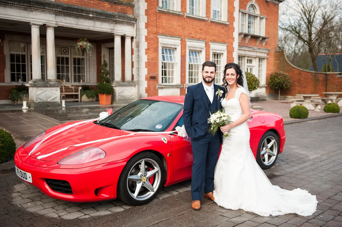 Bride and groom outside of Eaves Hall next to red Ferrari