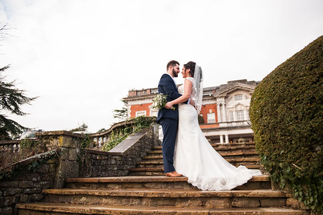 Bride and groom on the steps at Eaves Hall with the wedding venue in the background.