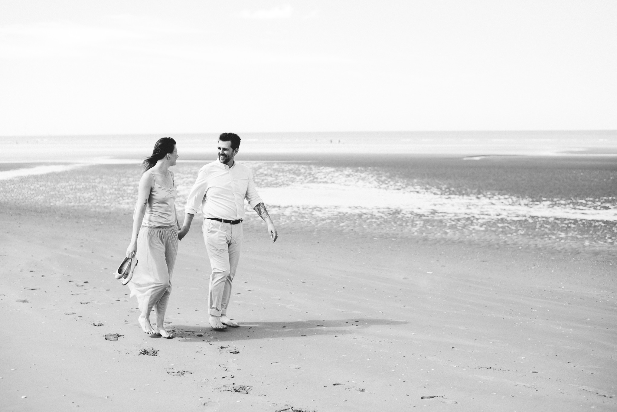 Bride and groom holding hands as they walk together along Formby beach.
