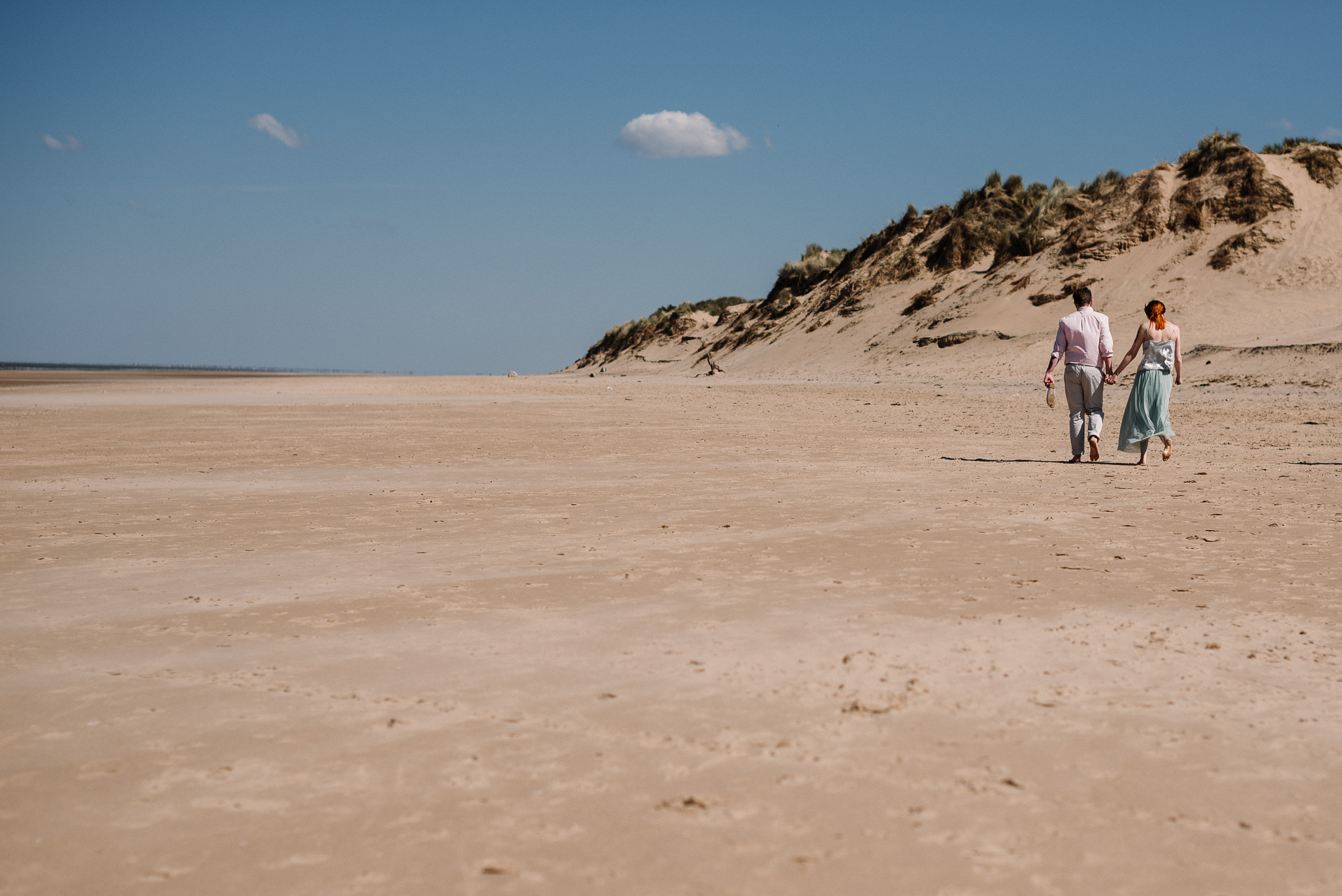 Natural shot of couple walking along the beach towards the sand dunes on Formby beach. 