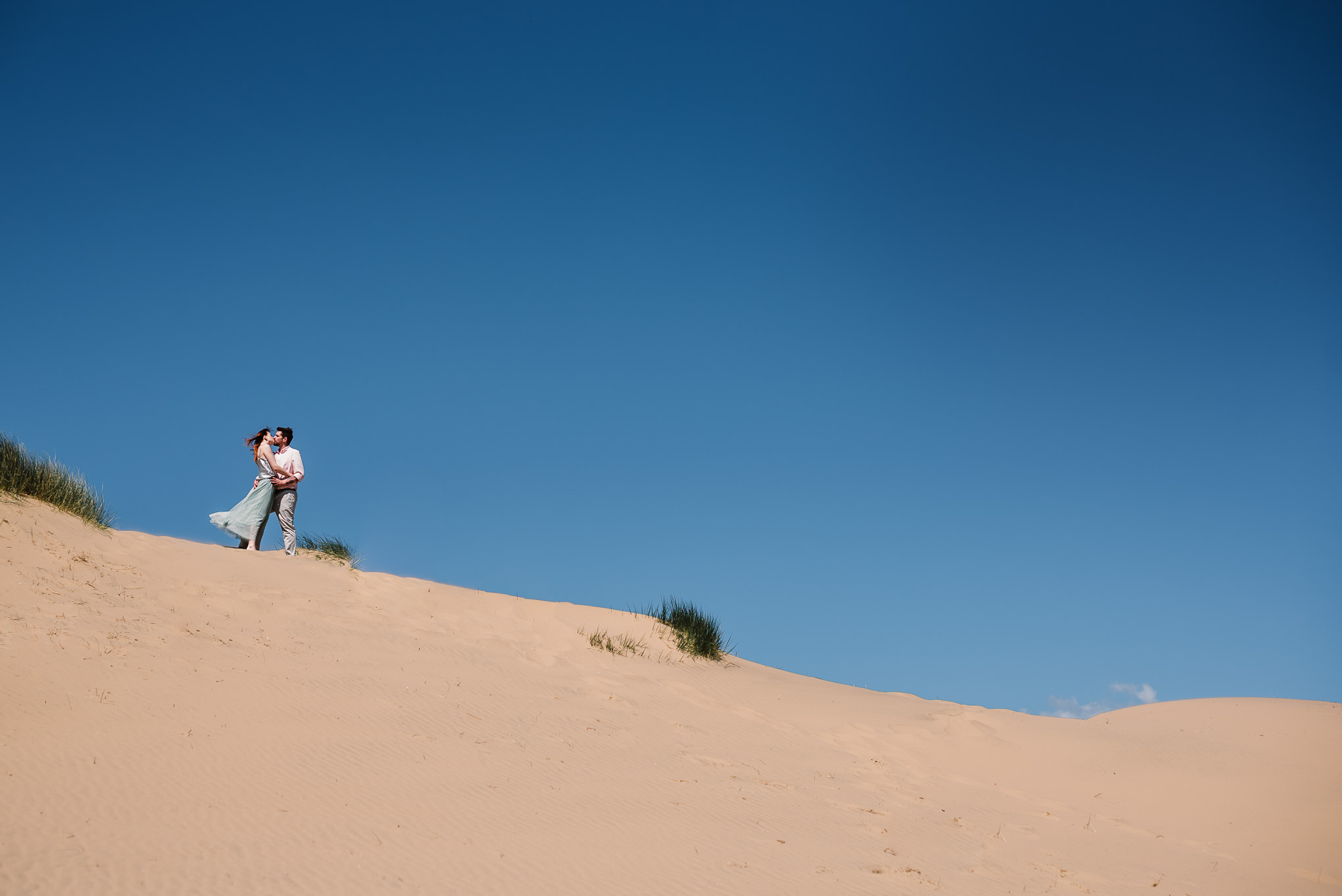 Landscape photo of bride and groom at the top of sand dune. Beach Wedding photography