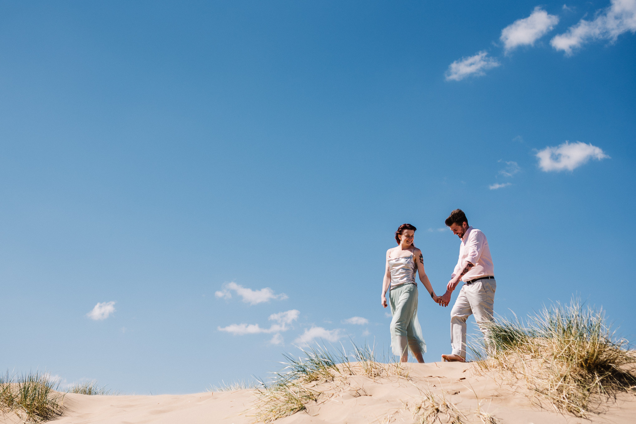 Bride and groom walking on hillside at Formby. Liverpool wedding photography