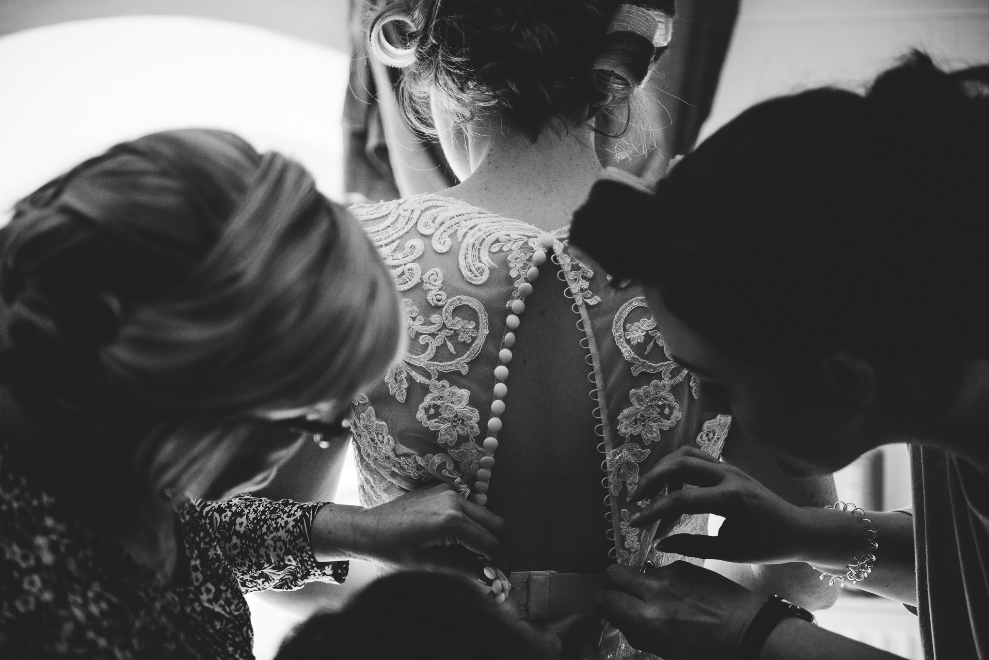 black and white photo of the brides wedding dress being buttoned up by her bridesmaids at the Dreamcatcher in Cornwall. 