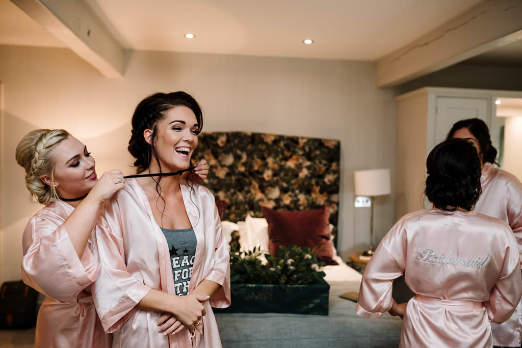 Bridesmaids helping each other to get dressed. Natural wedding photography