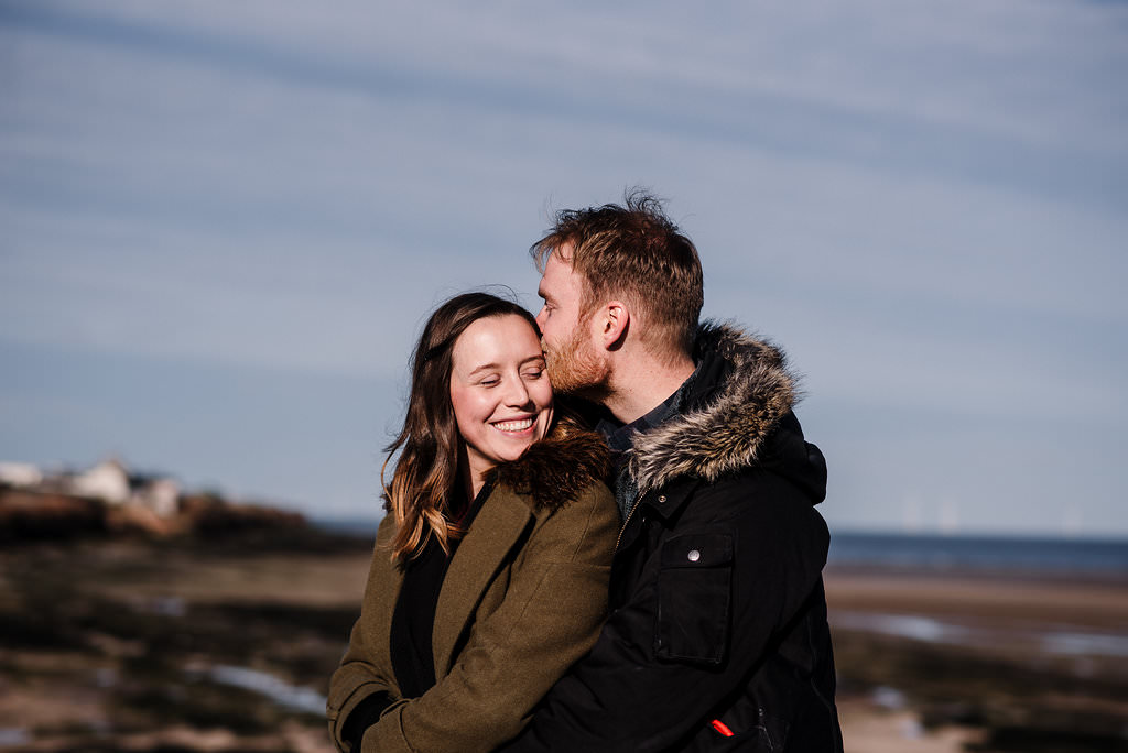 Couple hugging with landscape in the background. West Kirby engagement photography