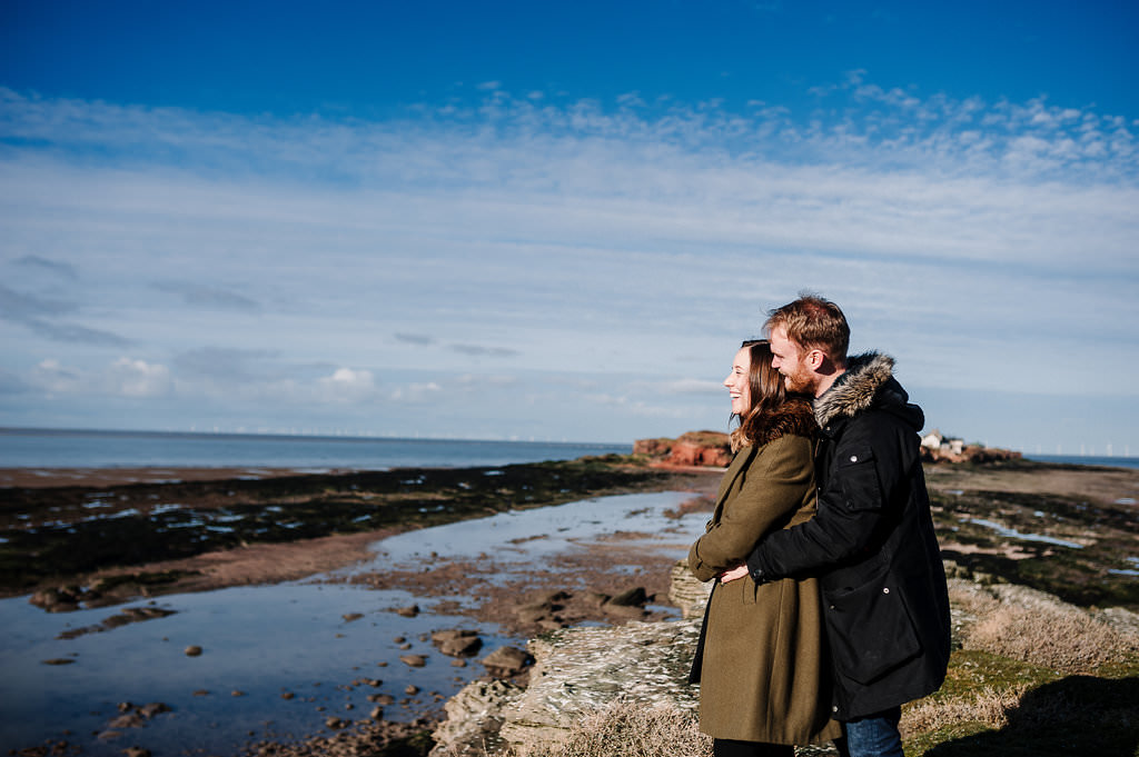 Relaxed photo of couple looking out to sea with Hilbre Island in the distance.
