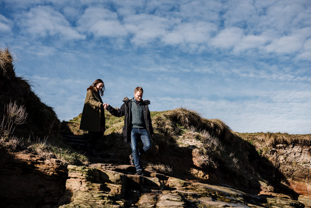 Couple walking down hillside together. Natural engagement photography