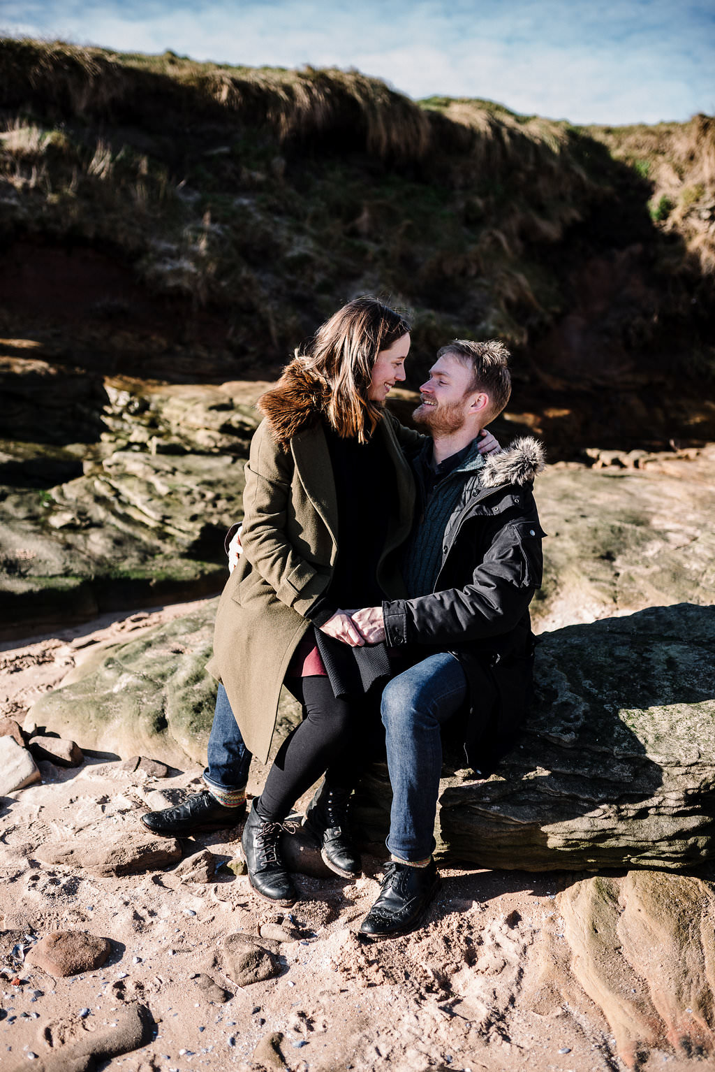 Intimate portrait of couple sat on rocks kissing. Engagement photography 